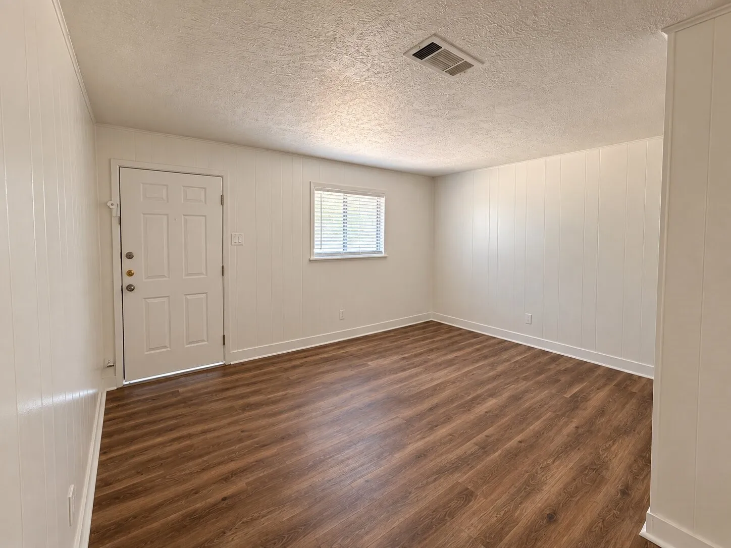 Wood-finish flooring with white baseboards, vertical paneling, and a panel door with multiple lites