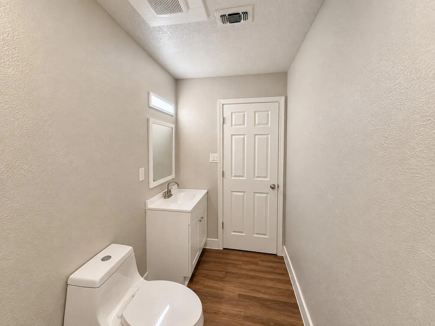 White vanity with an integrated sink, framed mirror, and wood-finish flooring