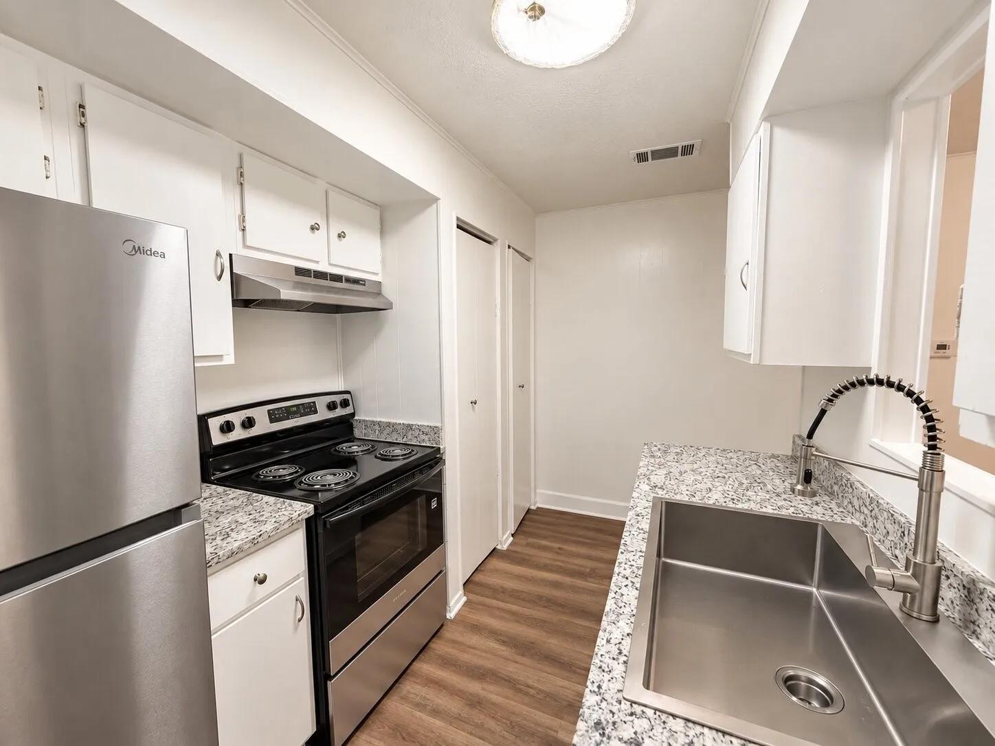 Stainless steel appliances, granite-style countertops, wood-finish flooring, white cabinetry, and a large stainless steel sink