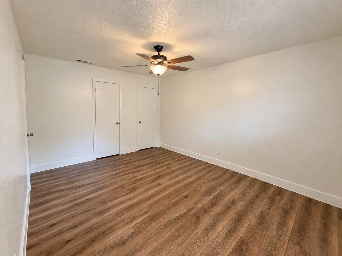 Wood-finish flooring, ceiling fan with integrated lighting, two white panel doors, and neutral wall tones
