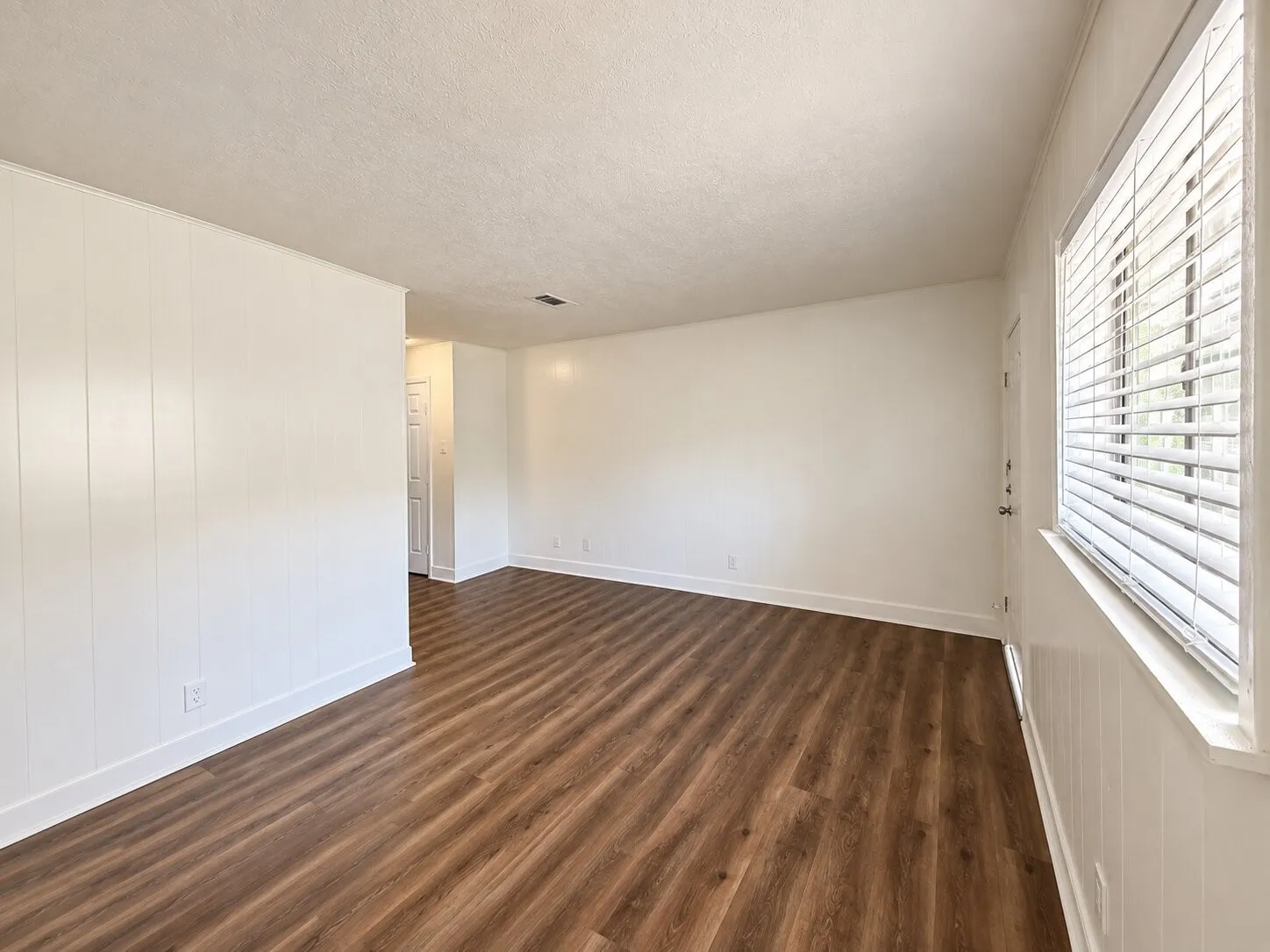 Wood-finish flooring, white paneled accent wall, white window blinds, and white trim throughout
