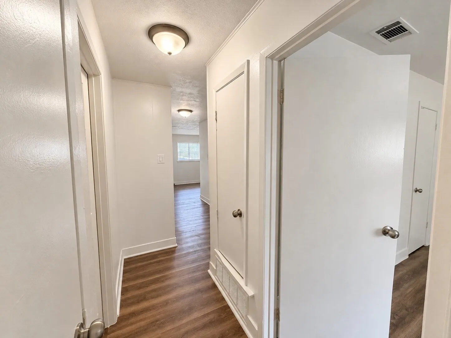Hallway featuring wood-finish flooring, white walls, and flush-mount lighting fixtures
