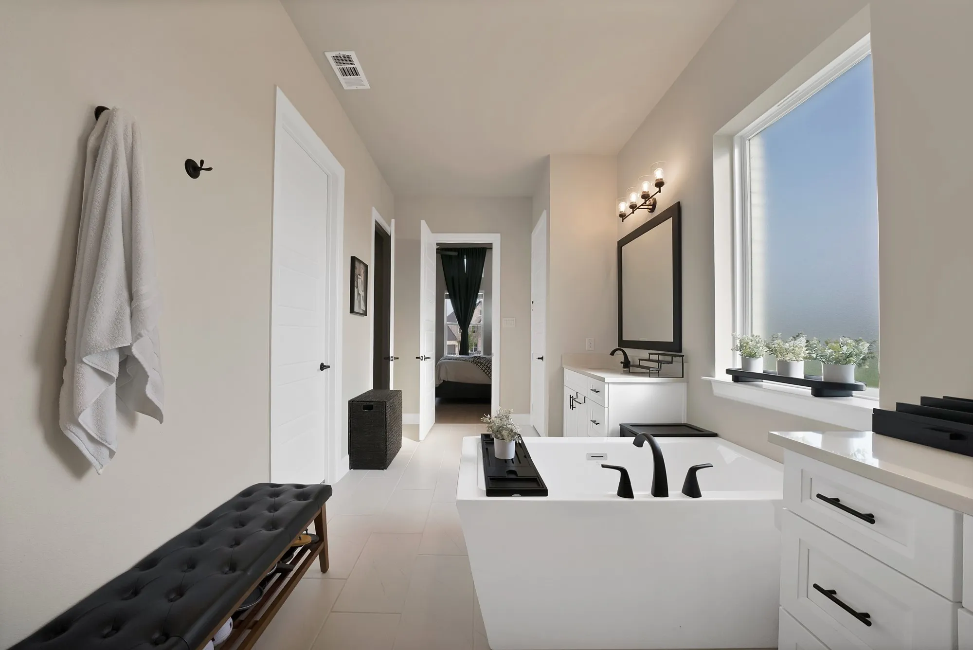 Freestanding soaking tub with matte black fixtures, dual white vanities with black hardware, and a large window providing ample natural light
