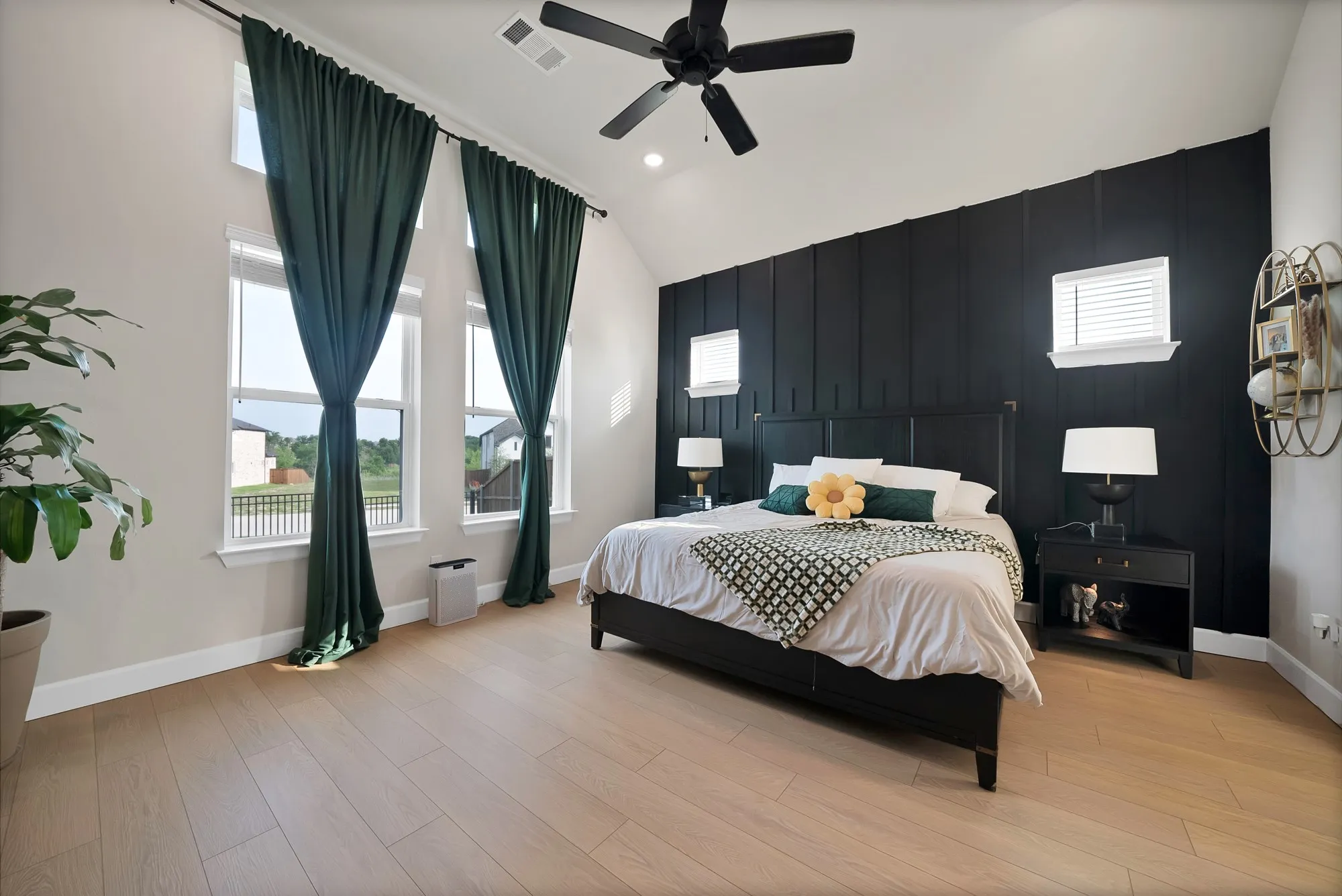 Vaulted ceiling with a ceiling fan, light wood-finish flooring, accent wall with vertical paneling, and multiple tall windows