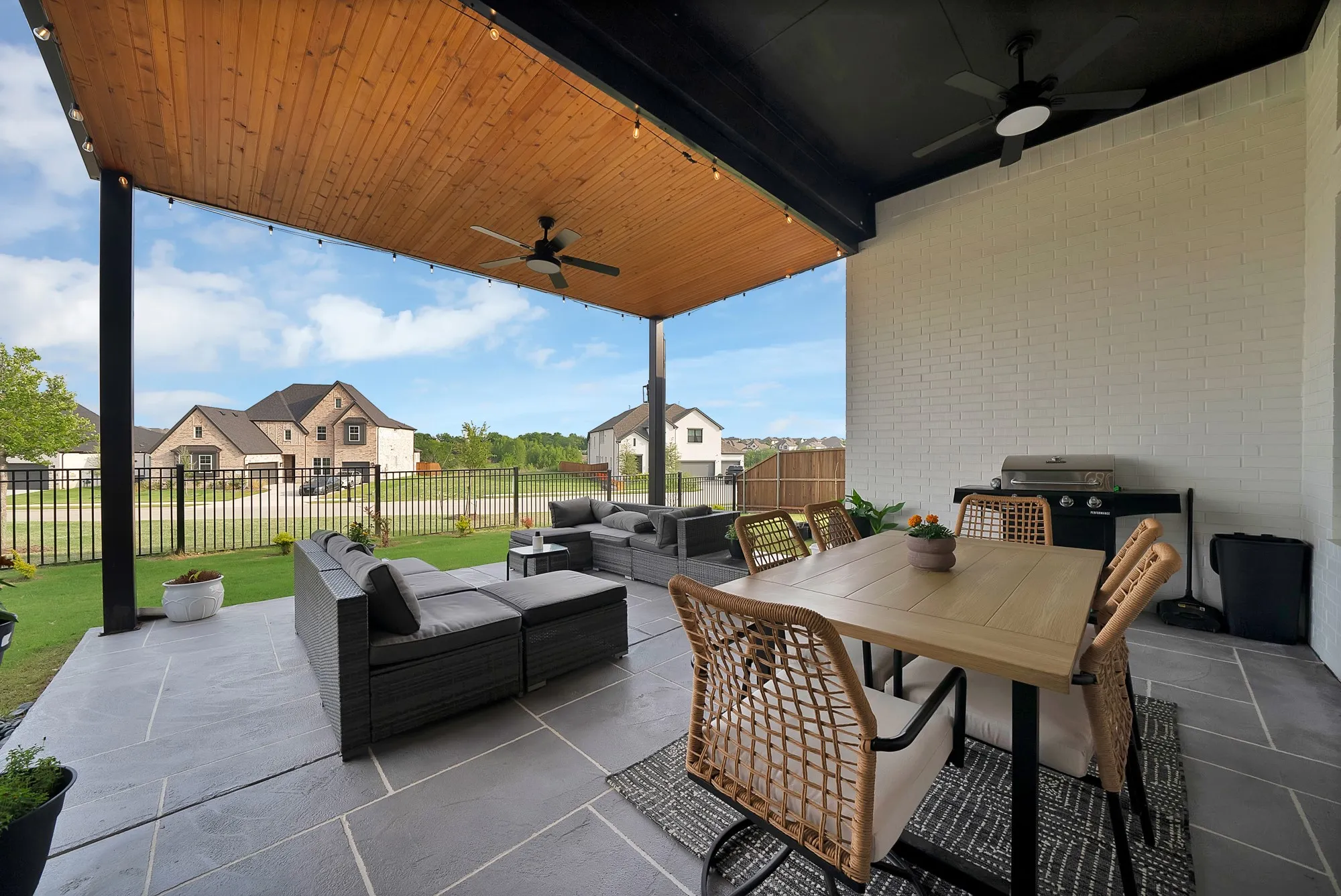 Covered outdoor patio with wood-finish ceiling, mounted ceiling fans, and an expansive stone-look tile floor