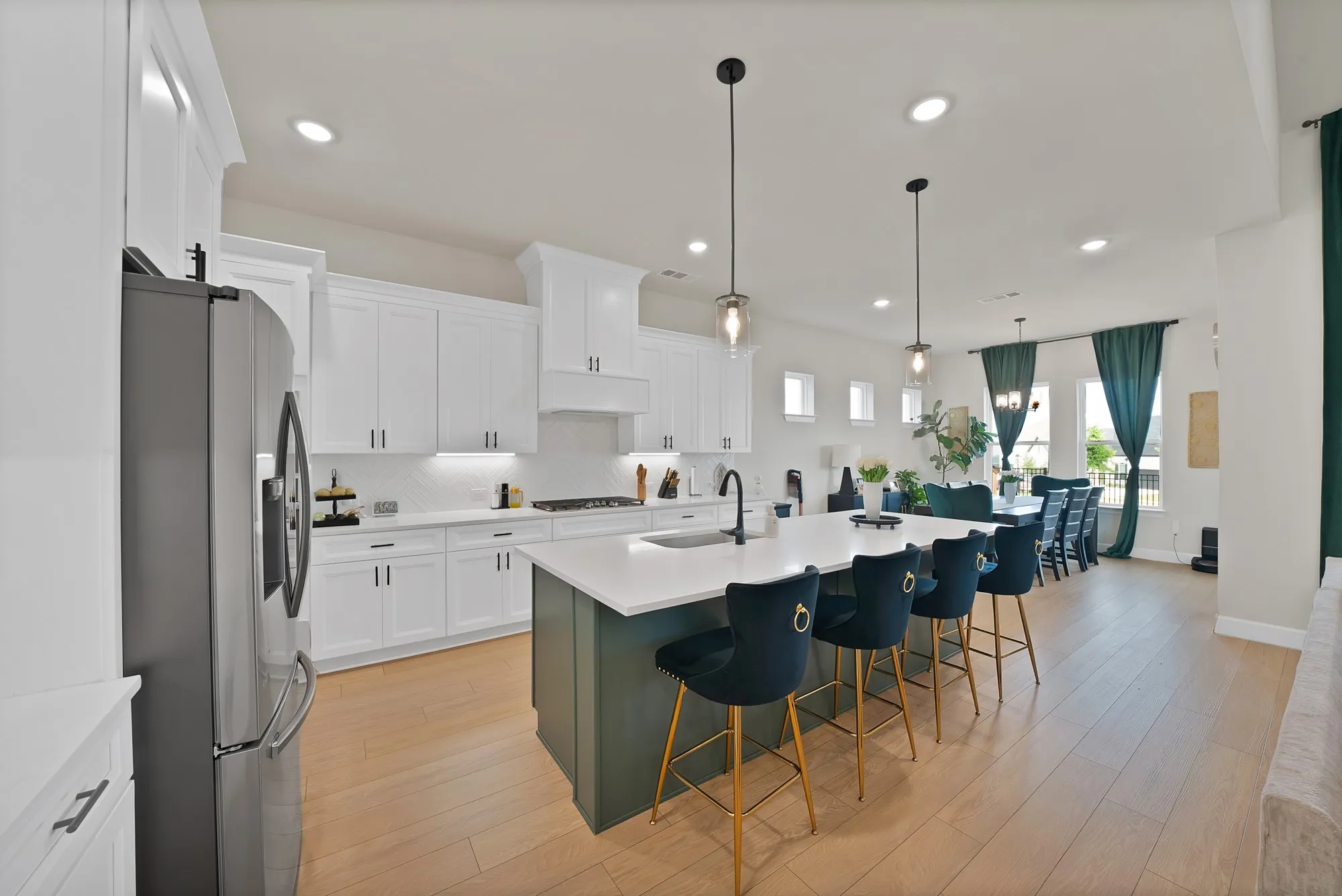 White shaker cabinetry, light wood-finish flooring, recessed lighting, stainless steel refrigerator, and a kitchen island with seating