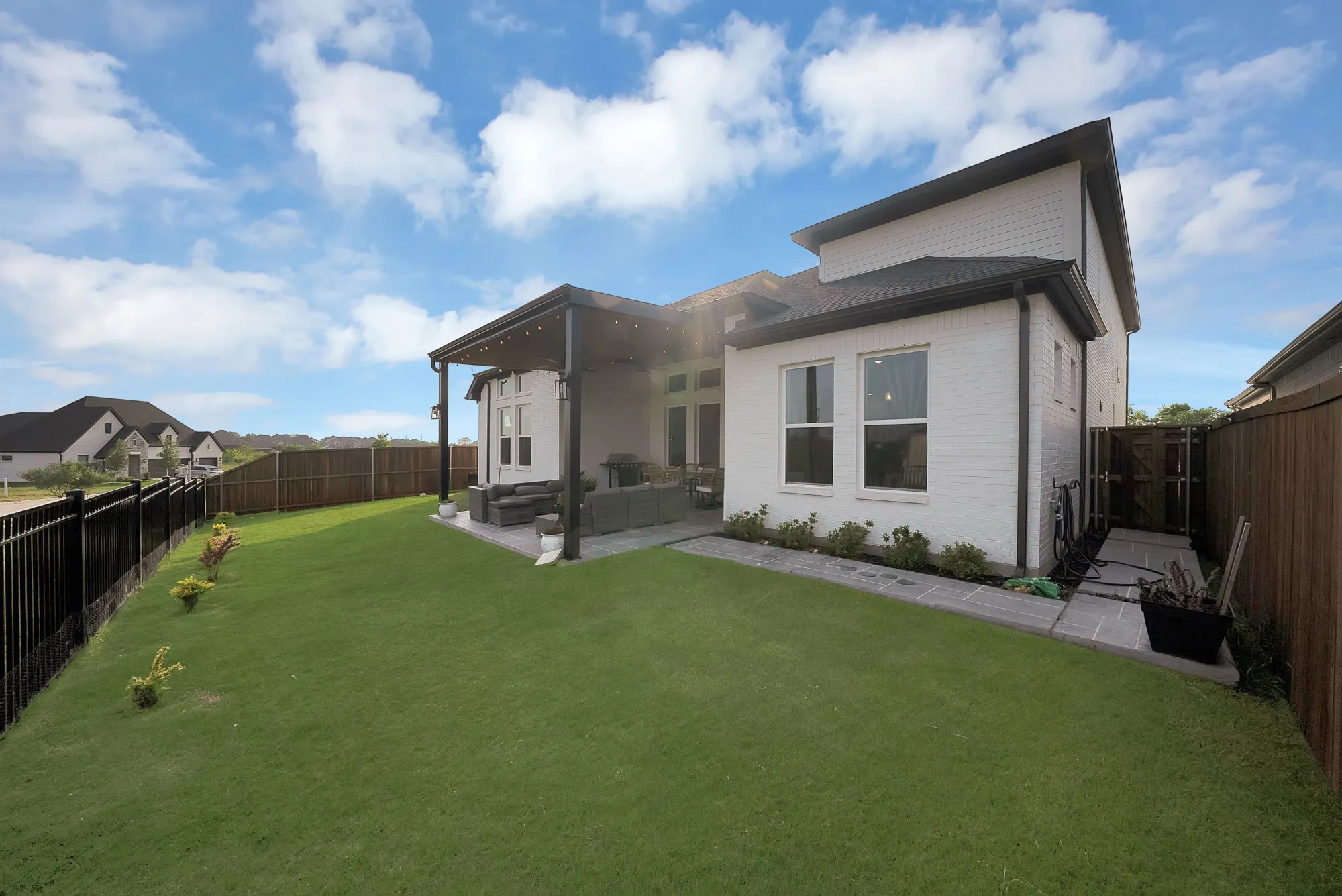 Expansive green lawn, white brick exterior, covered patio, metal fencing, and wood privacy fencing