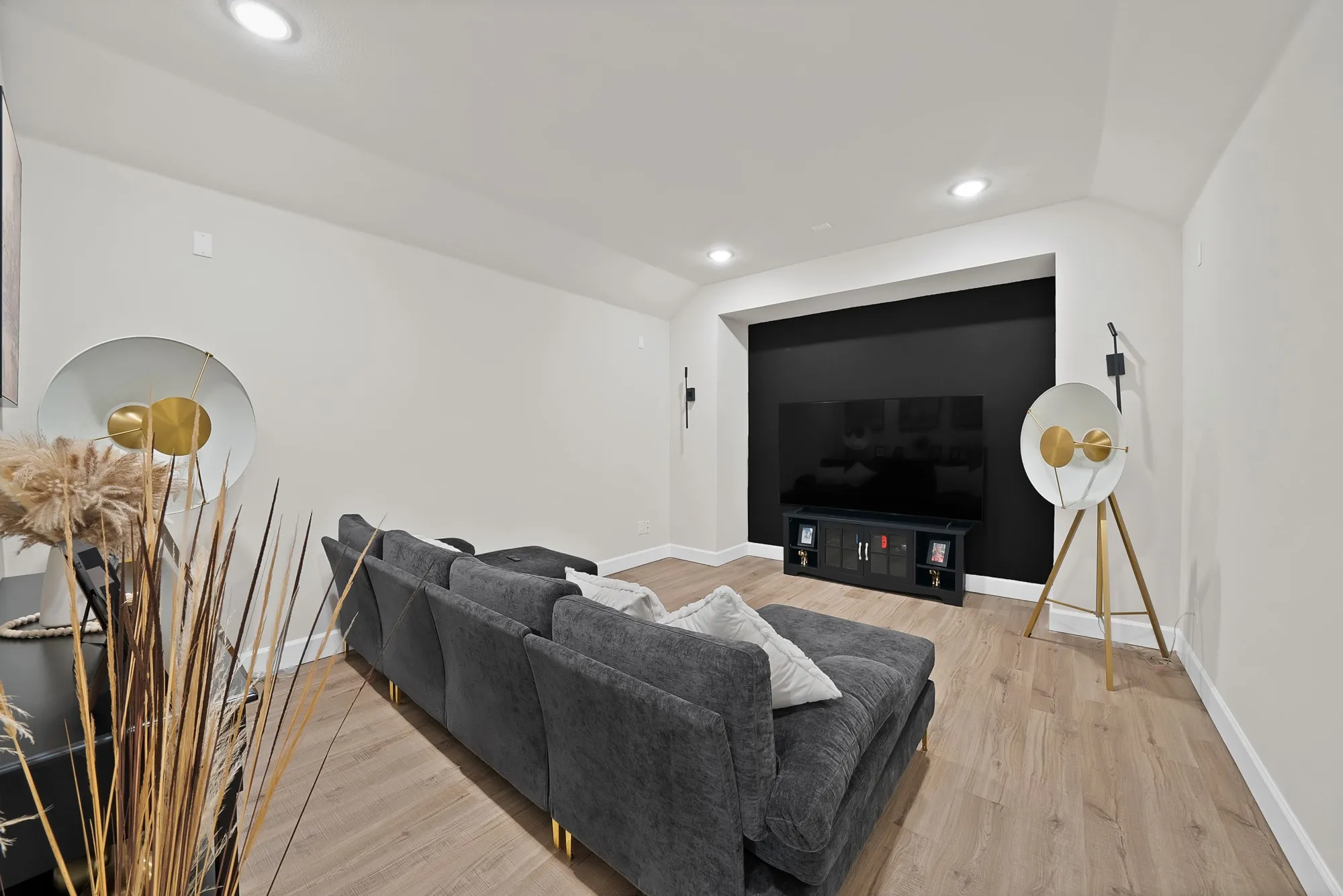 Recessed lighting, light wood-finish flooring, built-in media niche with dark accent wall, and wall-mounted sconces