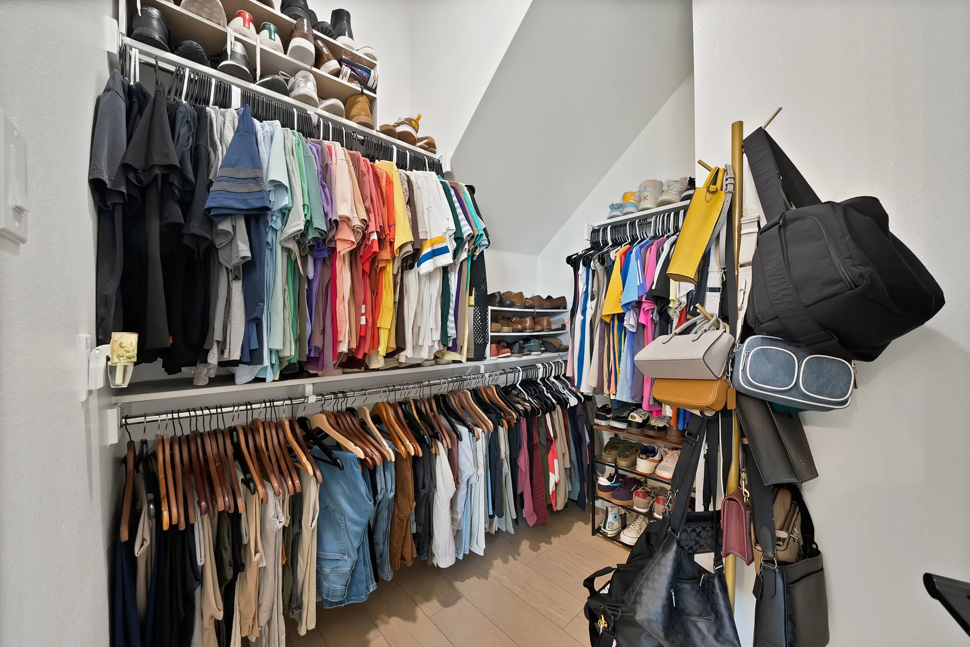Built-in closet system with multiple hanging rods, overhead shelving, and wood-finish flooring