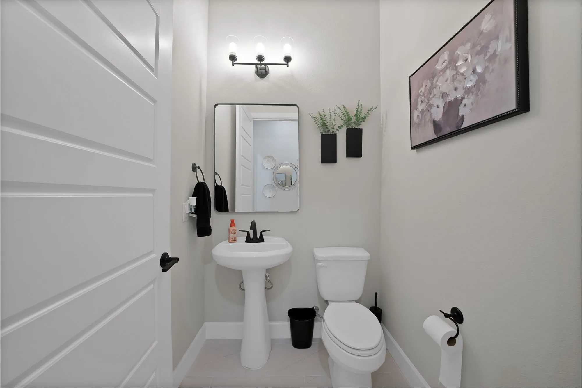 Pedestal sink with matte black faucet, framed mirror, and three-light vanity fixture