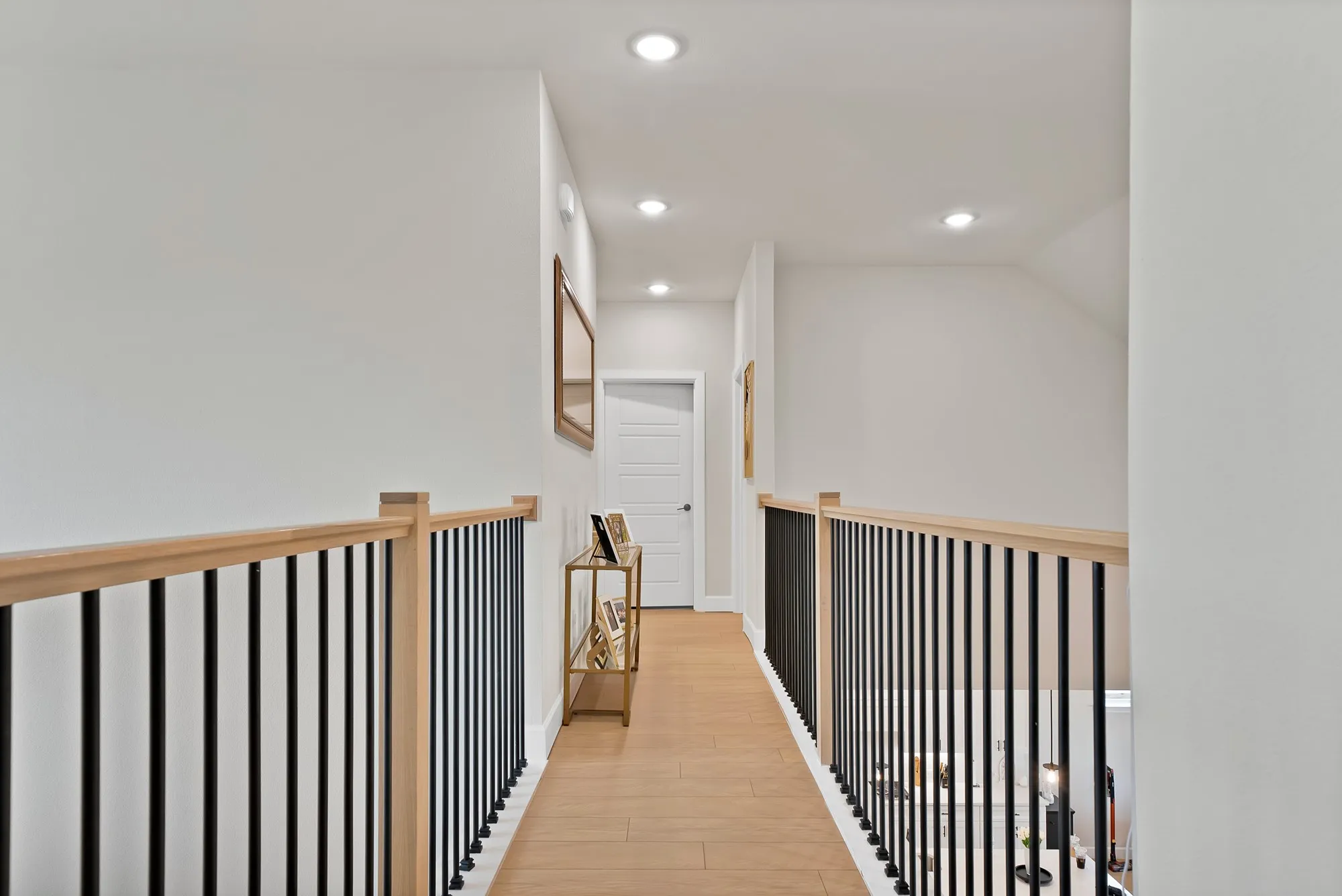 Hardwood-finish flooring, recessed ceiling lighting, light wood railings, and black metal balusters
