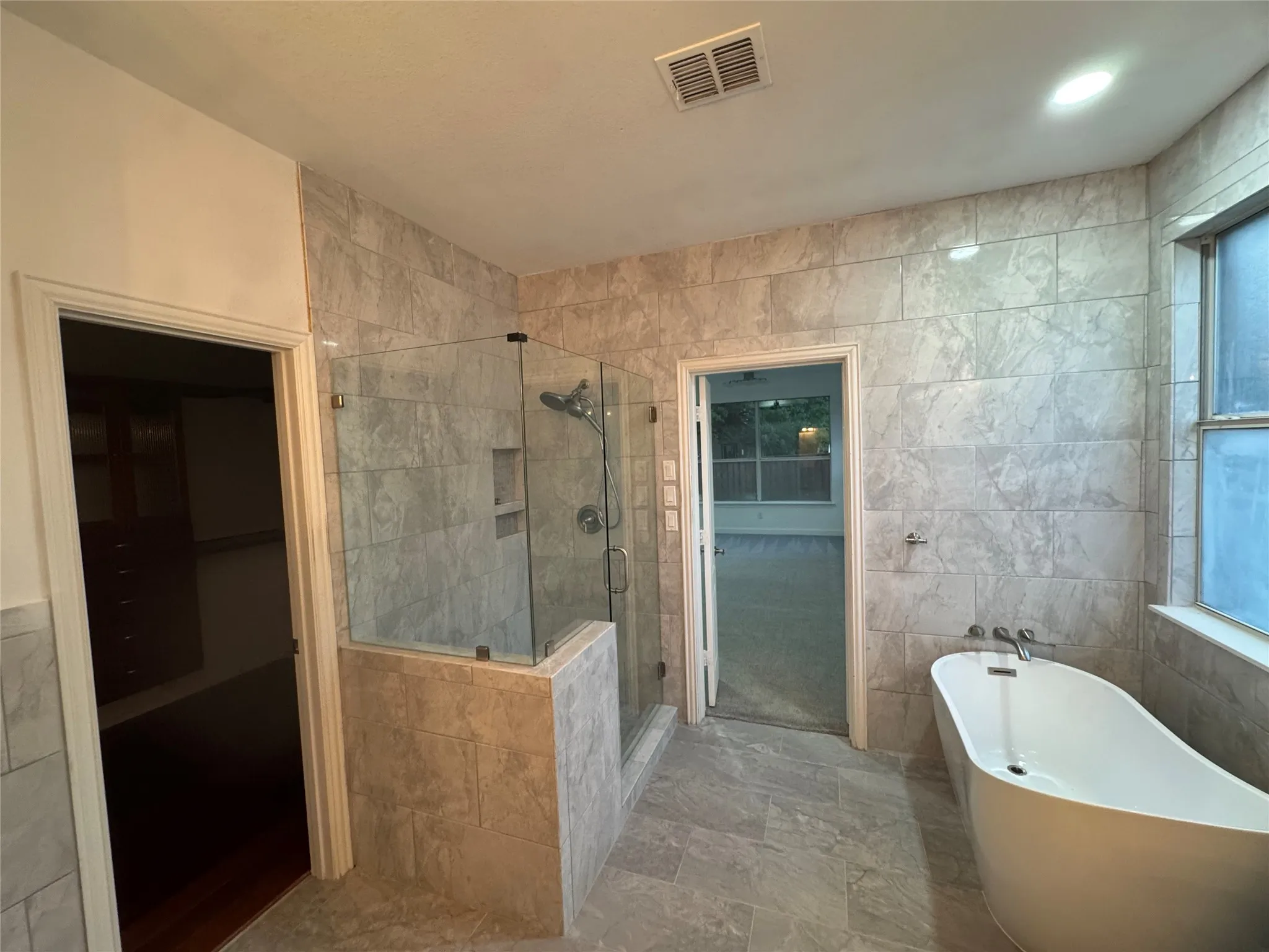 Freestanding soaking tub, walk-in shower with glass enclosure, recessed shower niche, and full-height tile walls