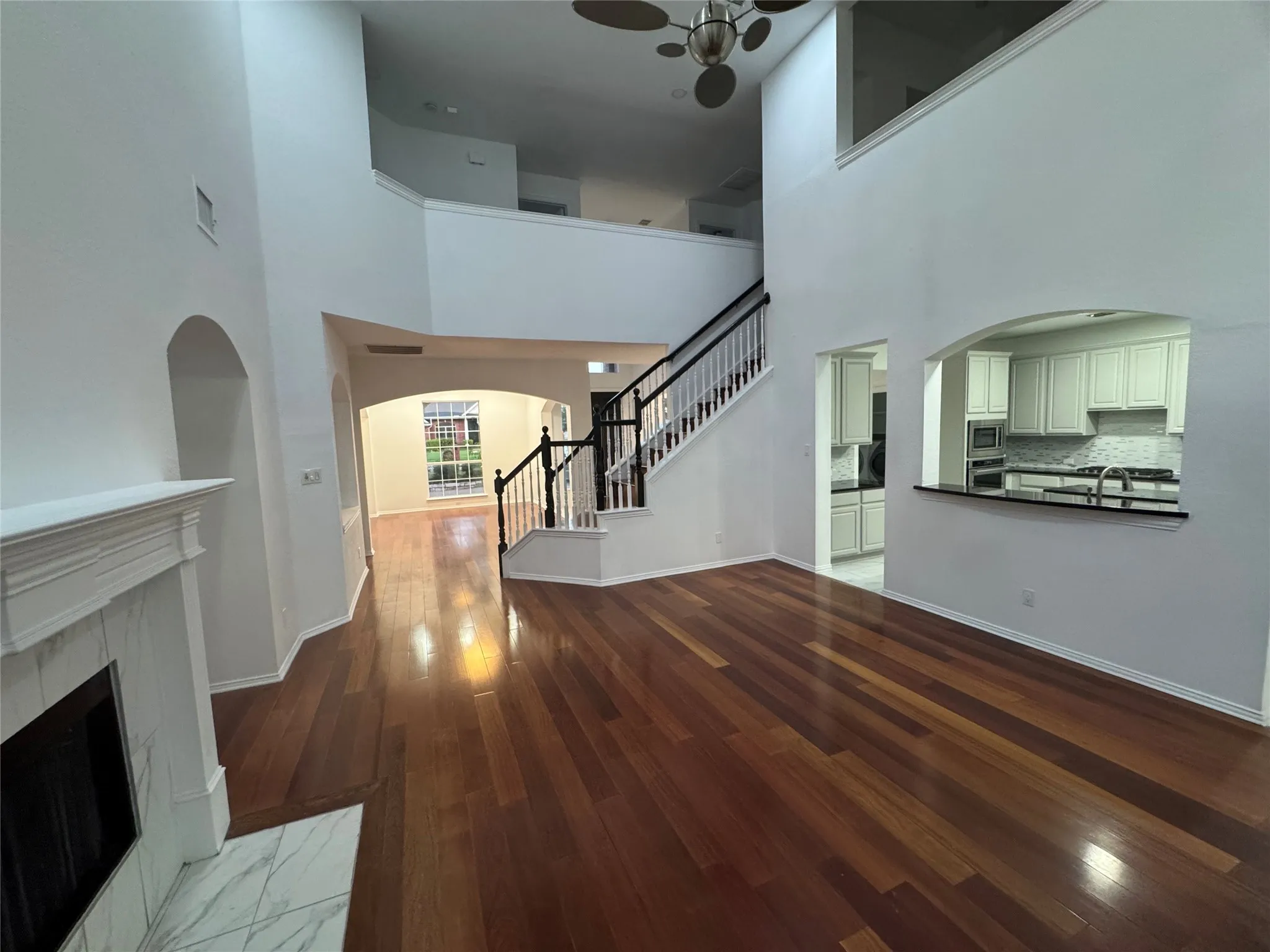 Soaring ceilings, rich wood-finish flooring, and a fireplace with a white mantel and marble-look surround