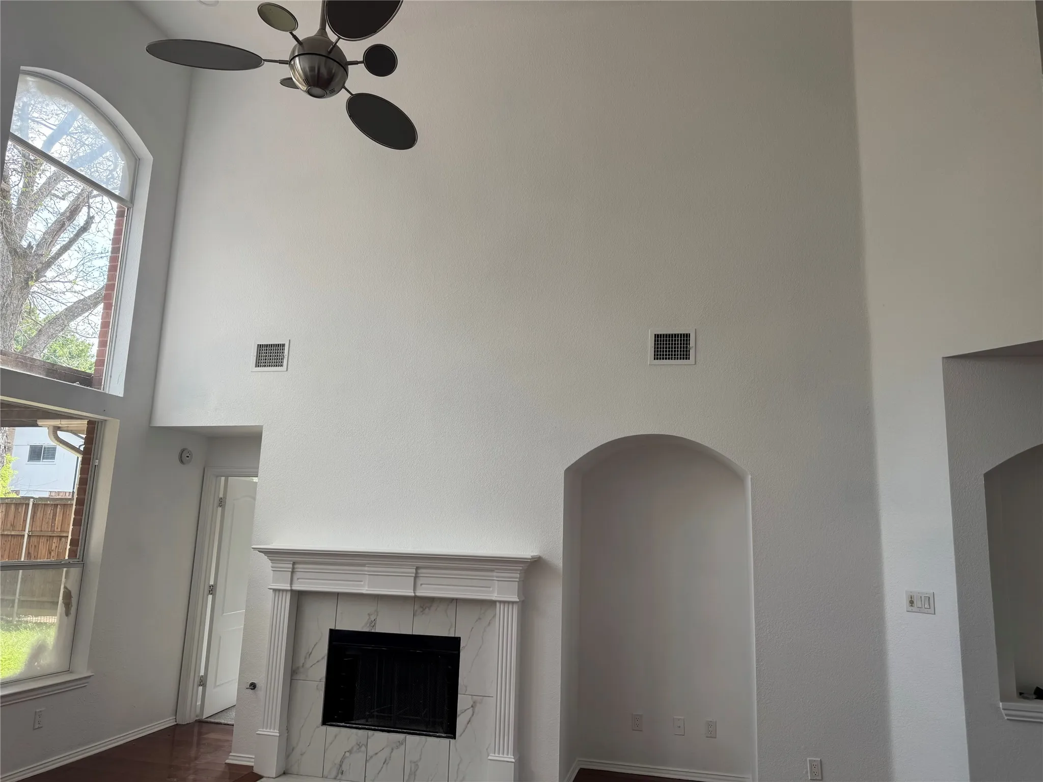 Two-story living area with a fireplace featuring a white mantel and marble-patterned surround