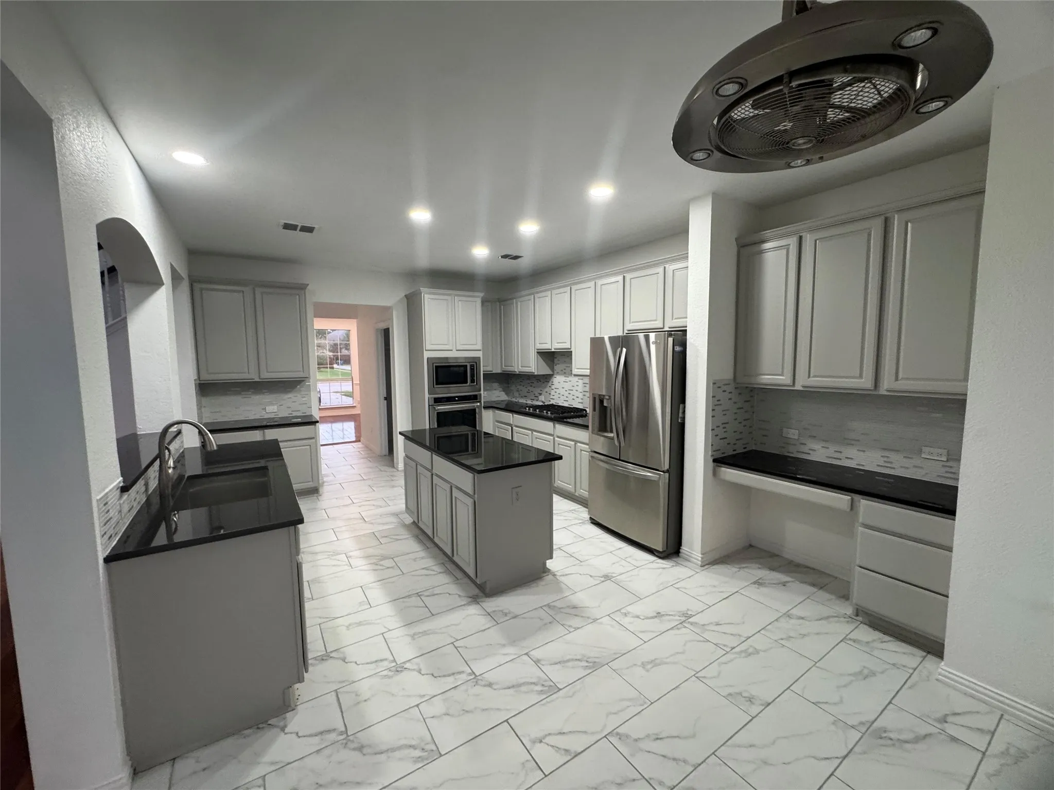 Spacious kitchen featuring an island, light gray cabinetry, dark countertops, a tiled backsplash, and stainless steel appliances