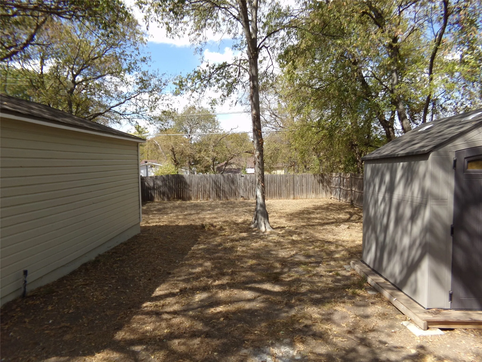 Fenced backyard featuring a detached storage shed and mature trees