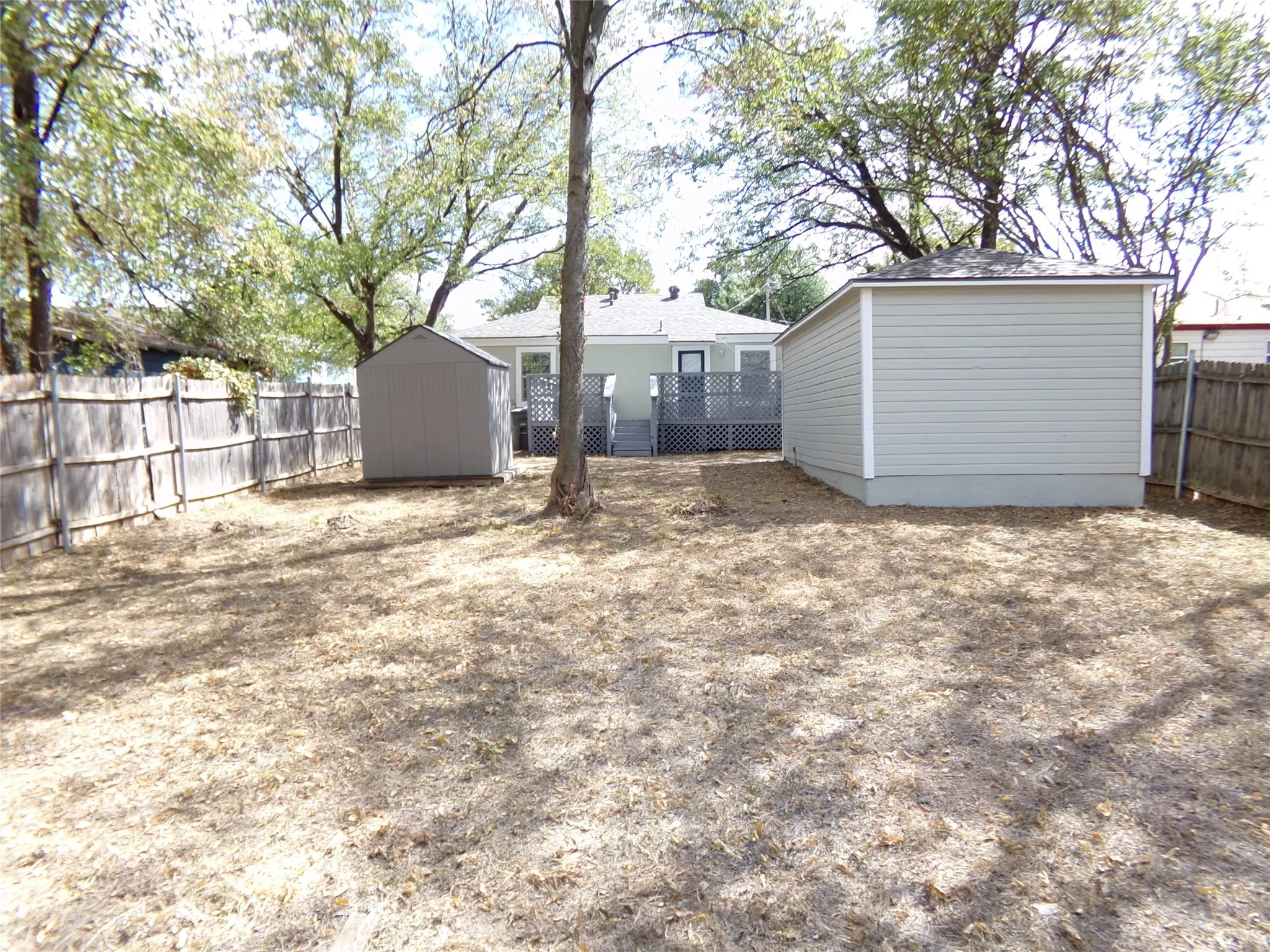 Expansive backyard featuring a privacy fence, two storage sheds, and a raised deck