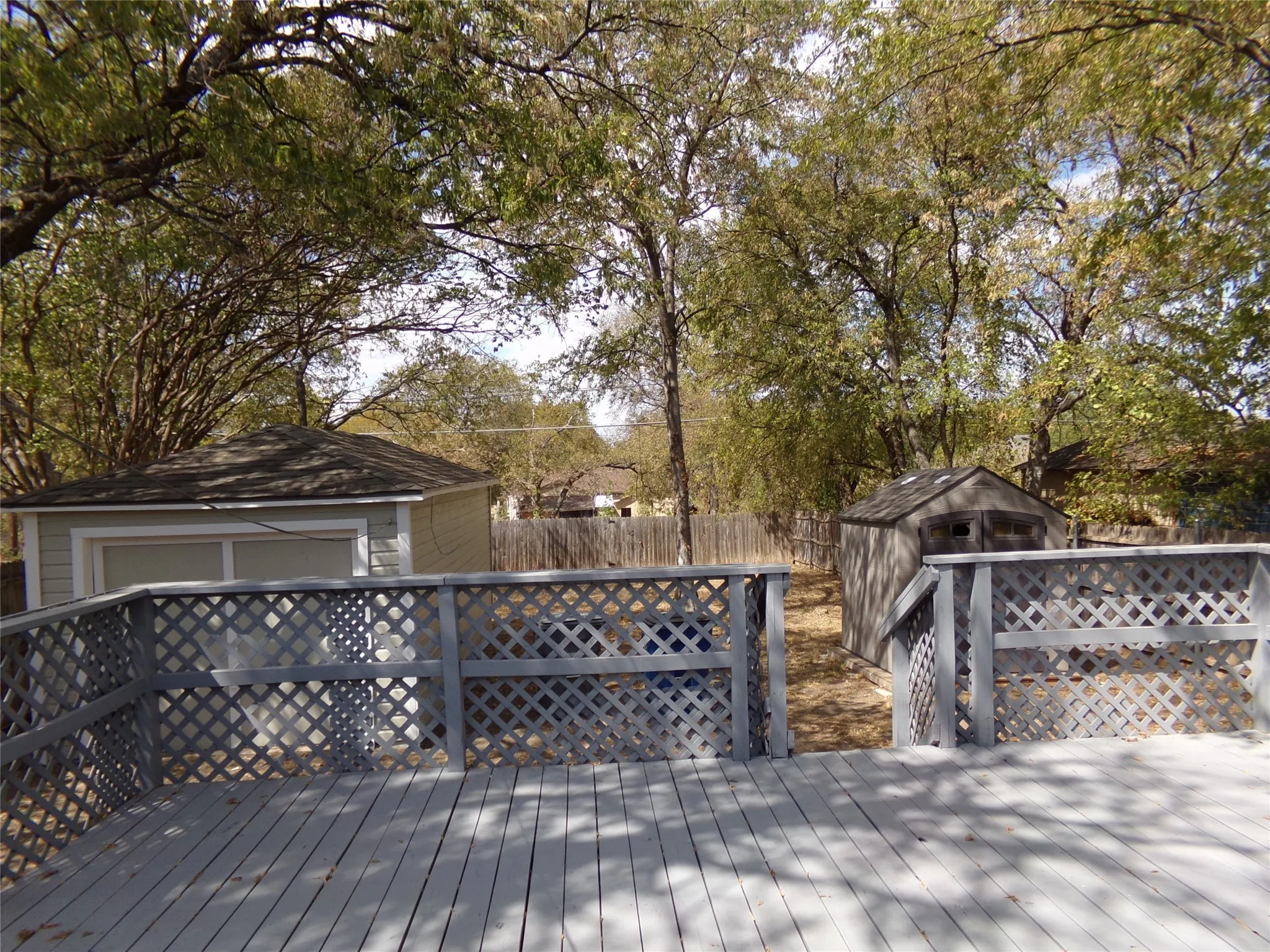 Spacious wood-plank deck with lattice railing, detached garage with shingle roof, and a separate storage shed