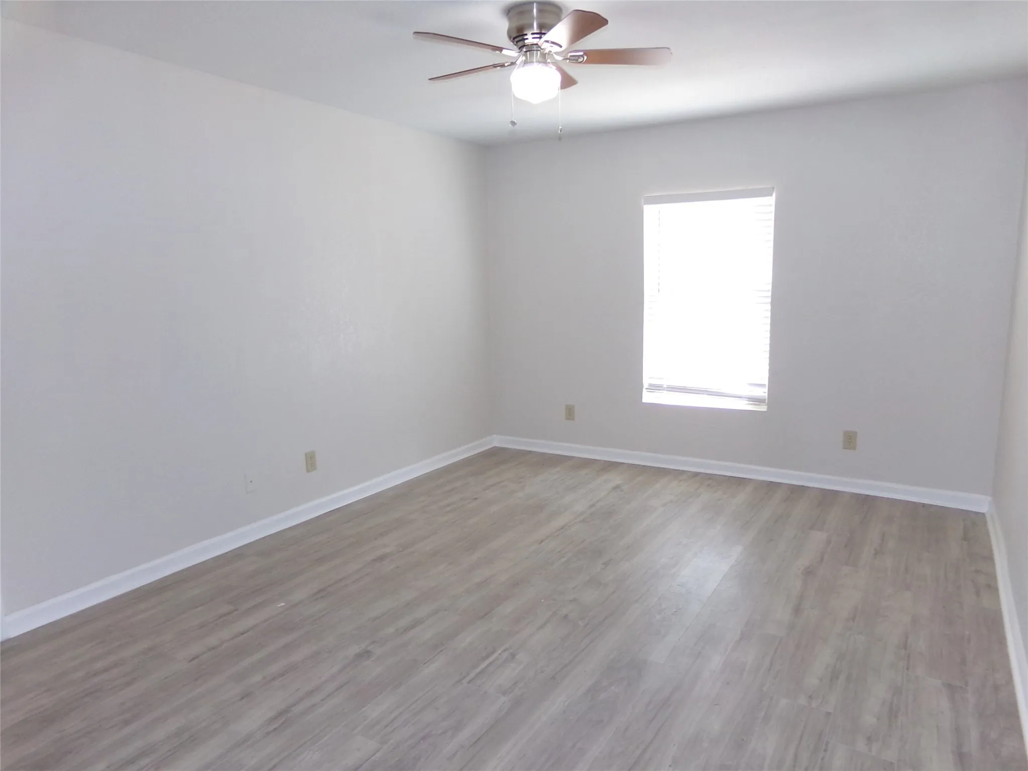 Recessed window with blinds, wood-finish flooring, ceiling fan with light fixture, and neutral wall tones