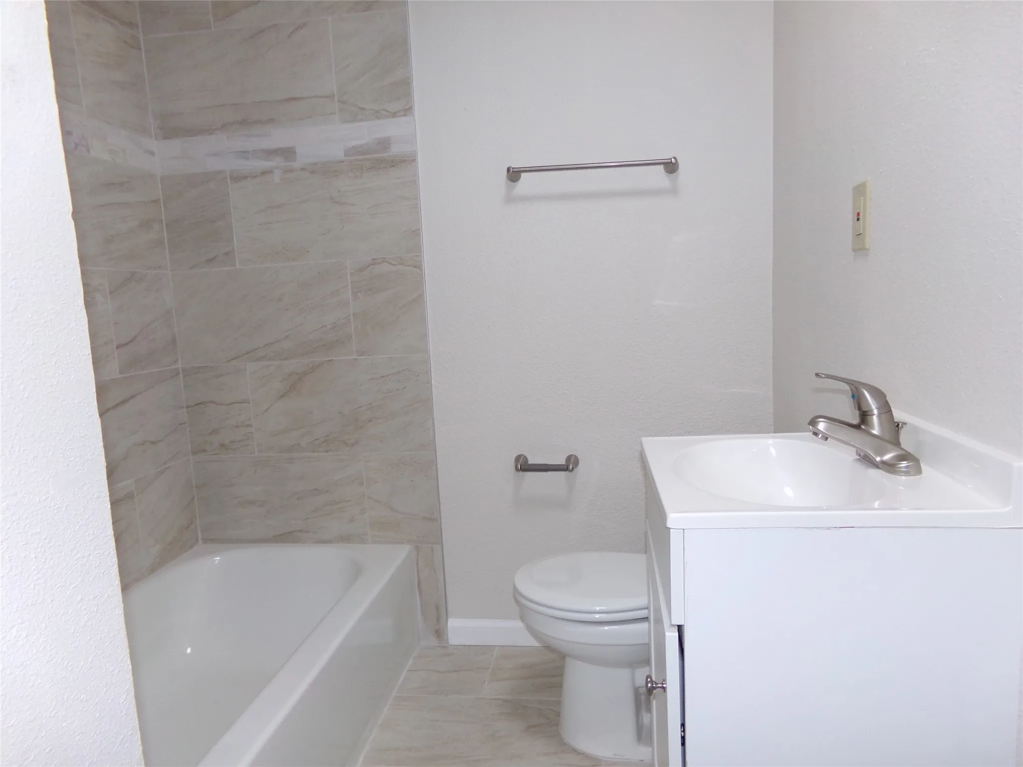 White tub with tiled surround, white vanity with integrated sink, and brushed nickel faucet