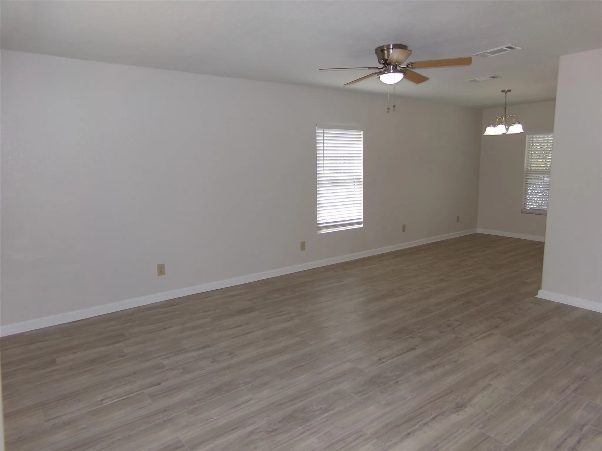 Neutral wall tones, wood-finish flooring, ceiling fan, natural light from multiple windows, and a chandelier-style light fixture