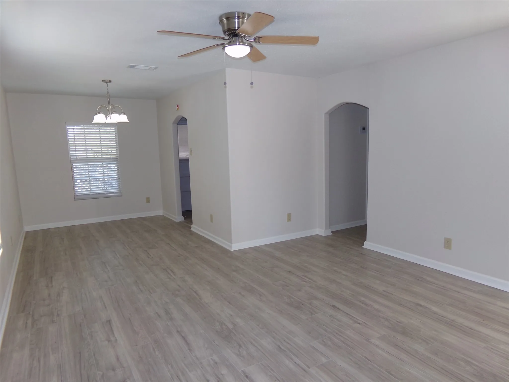 Expansive interior space featuring wood-finish flooring, a ceiling fan with integrated lighting, and a window with horizontal blinds