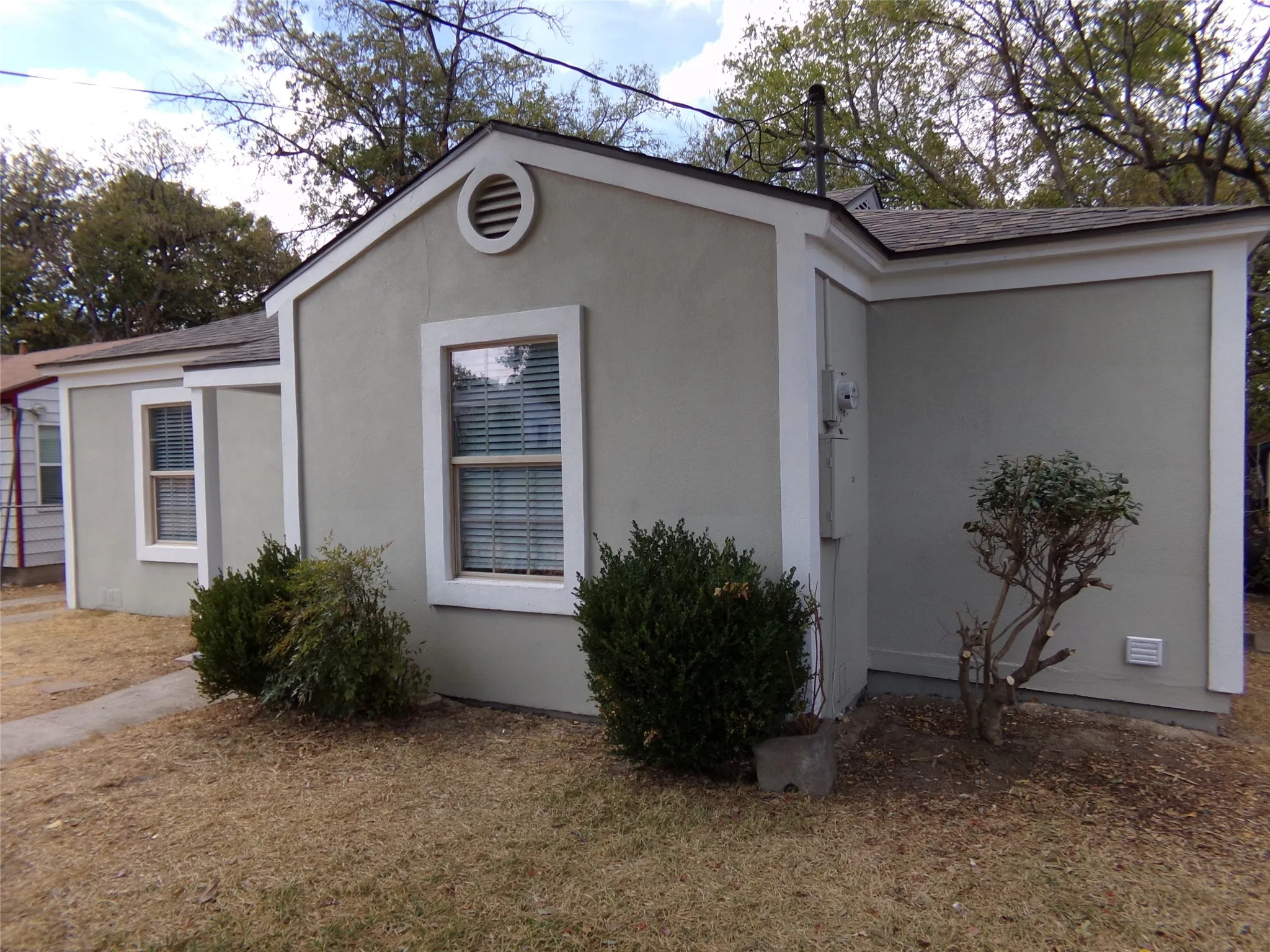 Stucco exterior with white trim, featuring multiple windows with blinds, and a circular gable vent