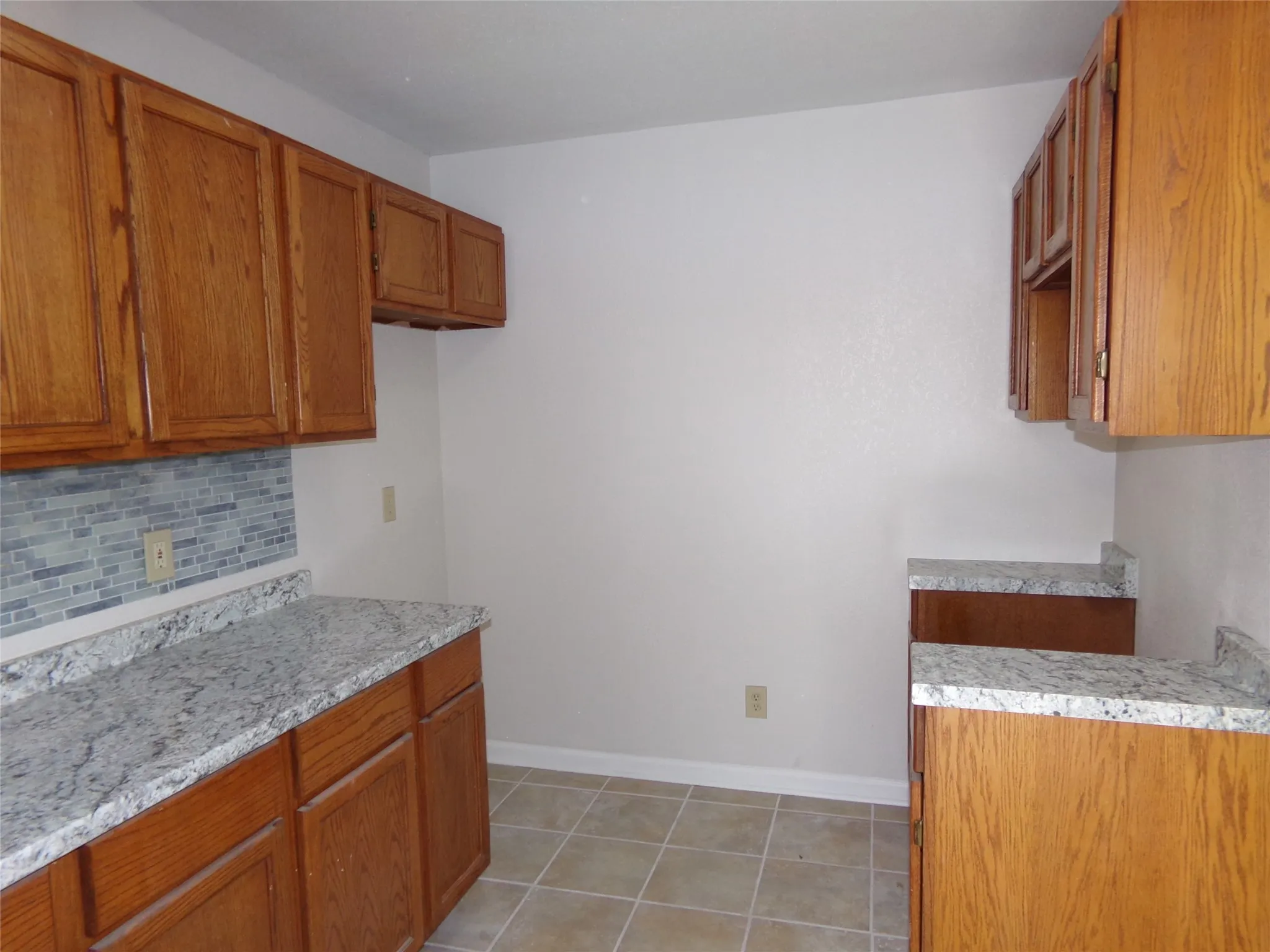 Wood cabinetry with sleek hardware, light-toned countertops, and a mosaic tile backsplash