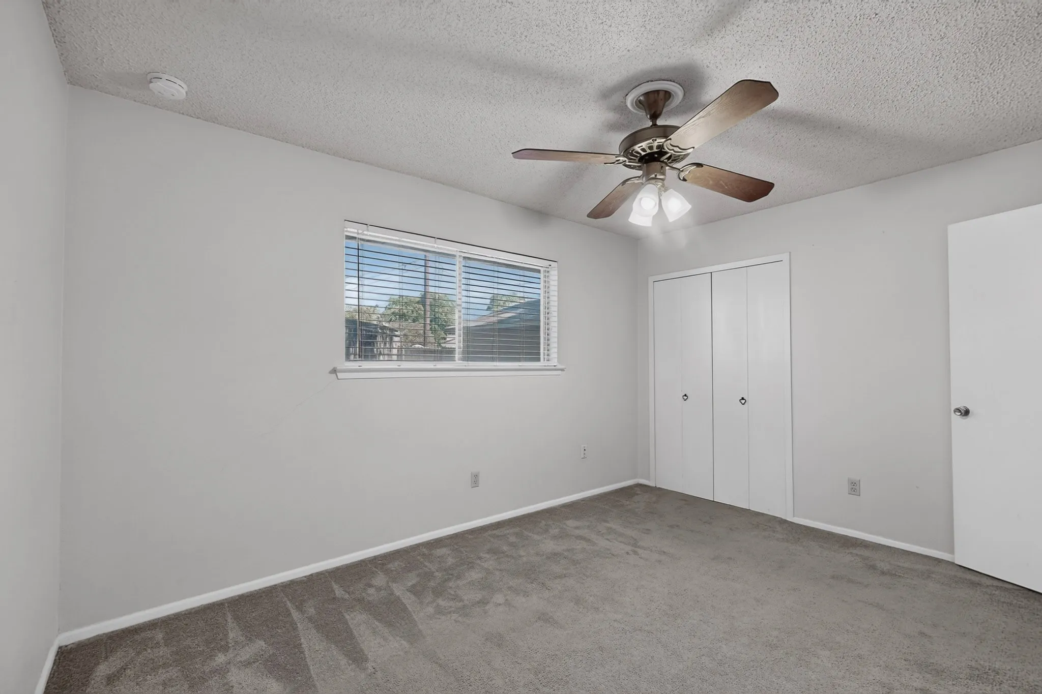 Wall-to-wall carpeting, window with blinds, ceiling fan with integrated lighting, and bi-fold closet doors