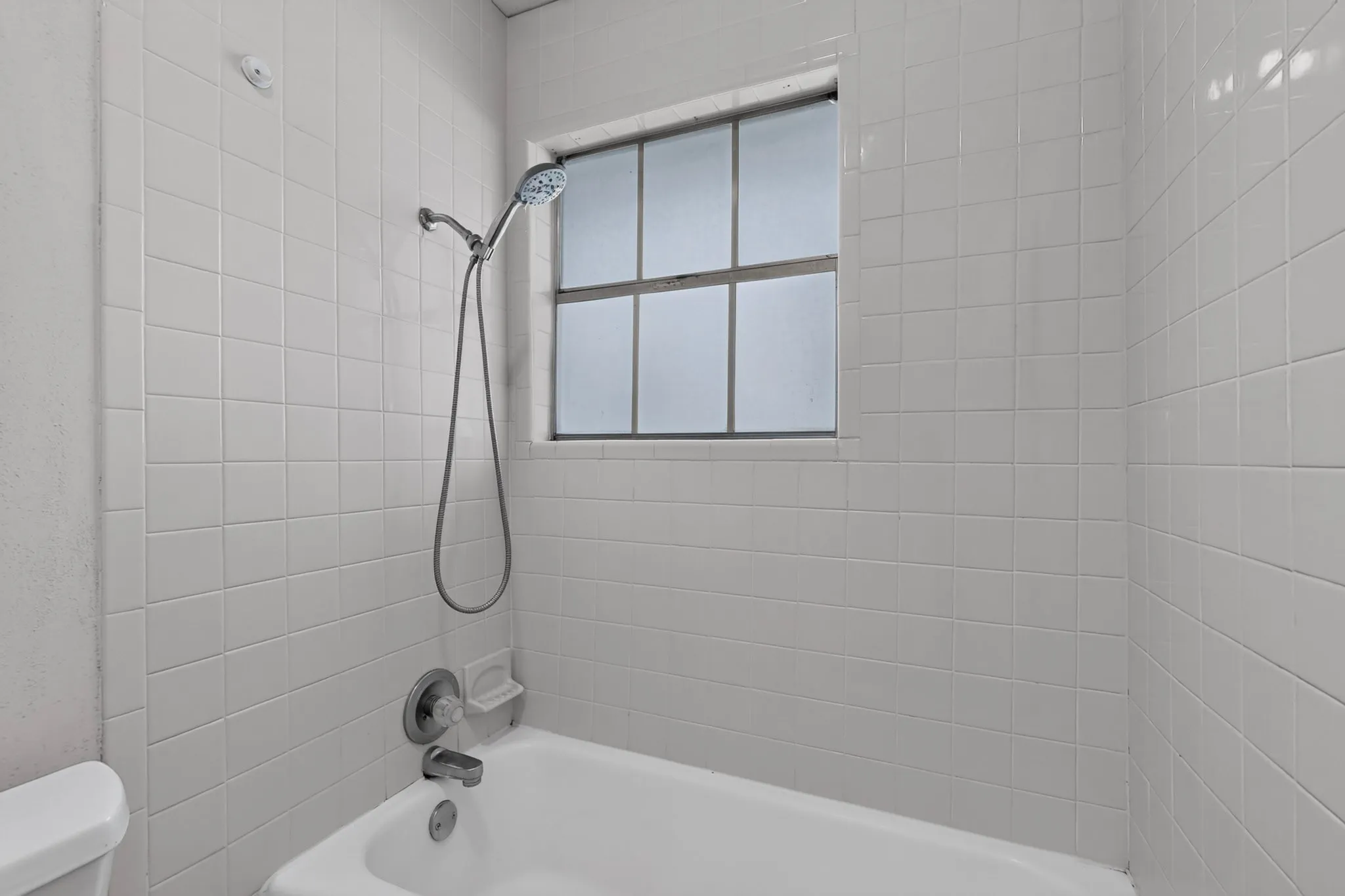 Tub and shower combination with white square tile surround, chrome fixtures, and a privacy window