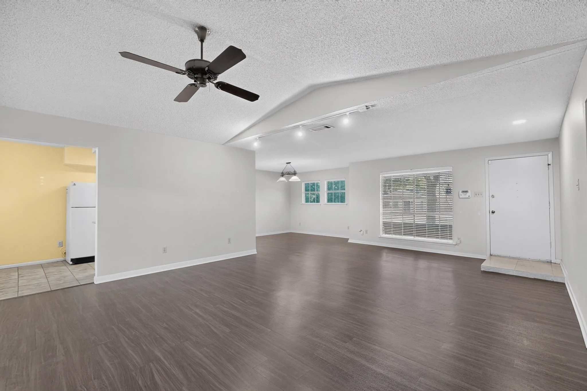 Vaulted ceiling with an installed ceiling fan, wood-finish flooring, two large windows, white walls, and track lighting
