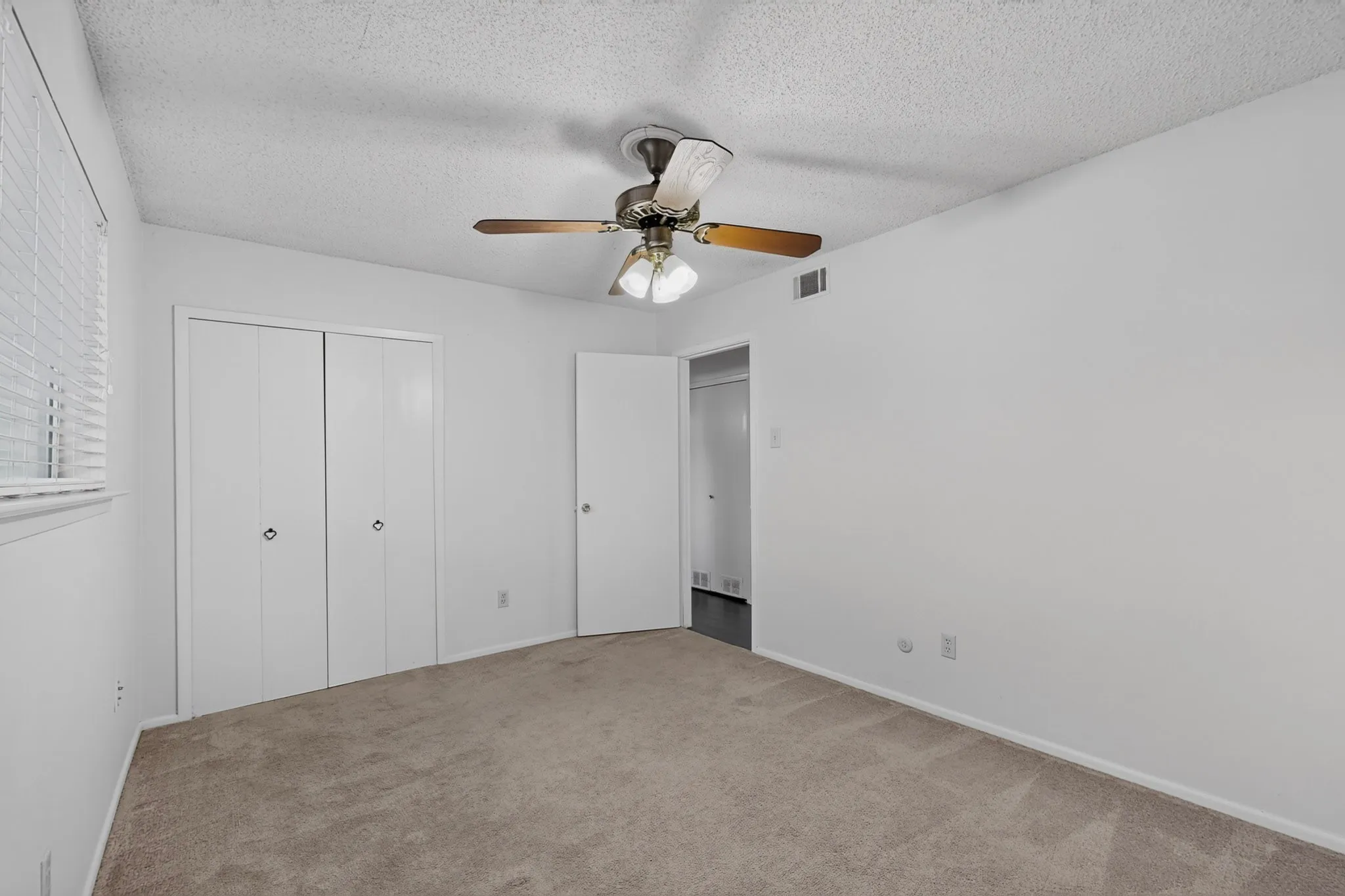 Neutral wall color, carpeted flooring, window with blinds, bi-fold closet doors, and a ceiling fan with integrated lighting