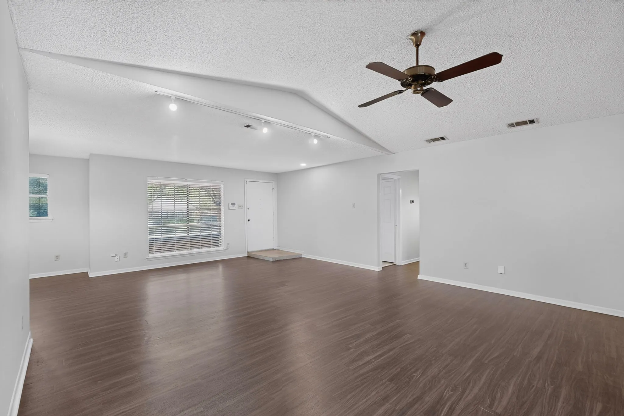 Vaulted ceiling featuring track lighting and a ceiling fan, wood-finish flooring, and a large front window