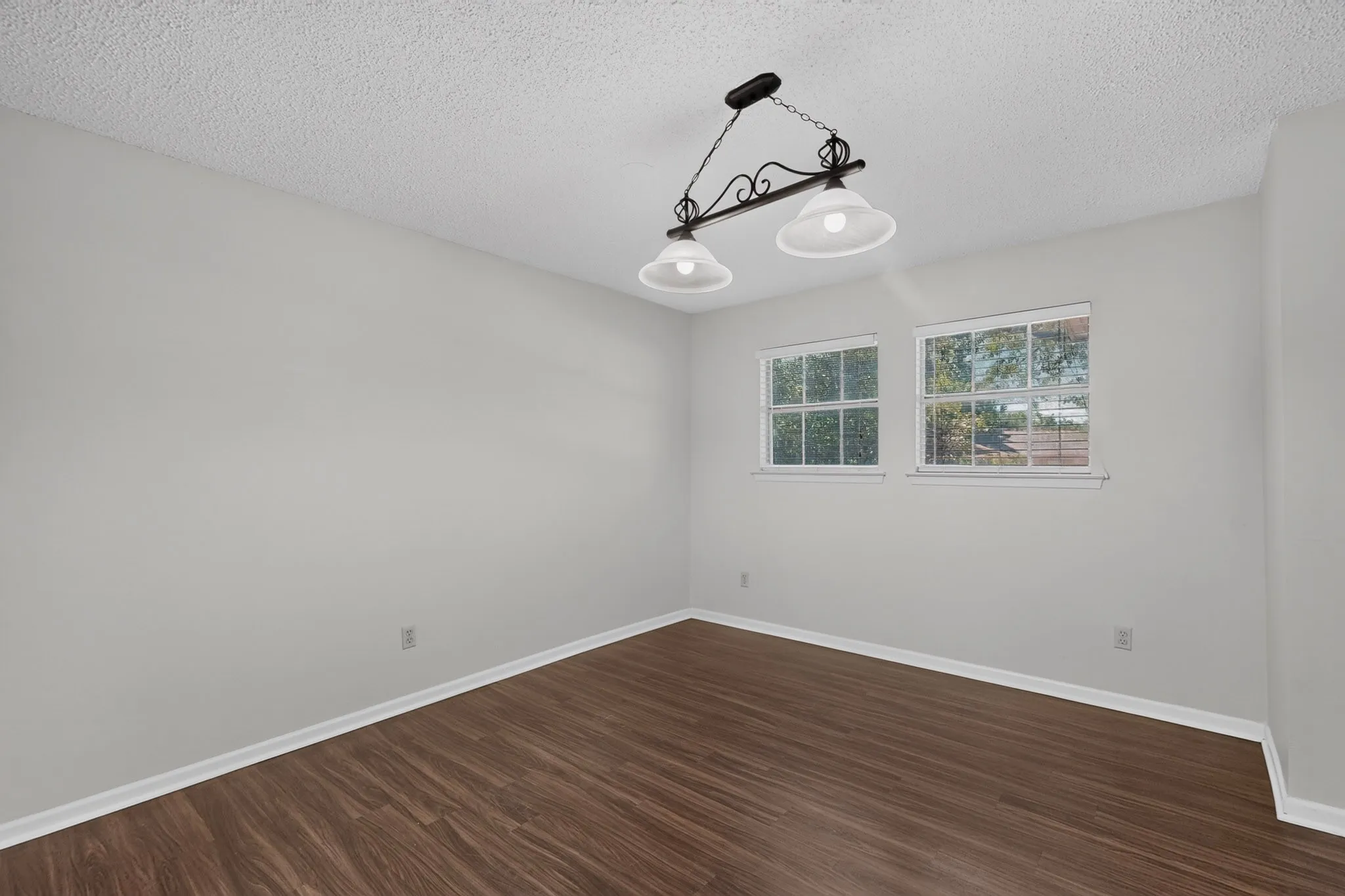Wood-finish flooring, white walls, two windows, and a multi-bulb ceiling fixture