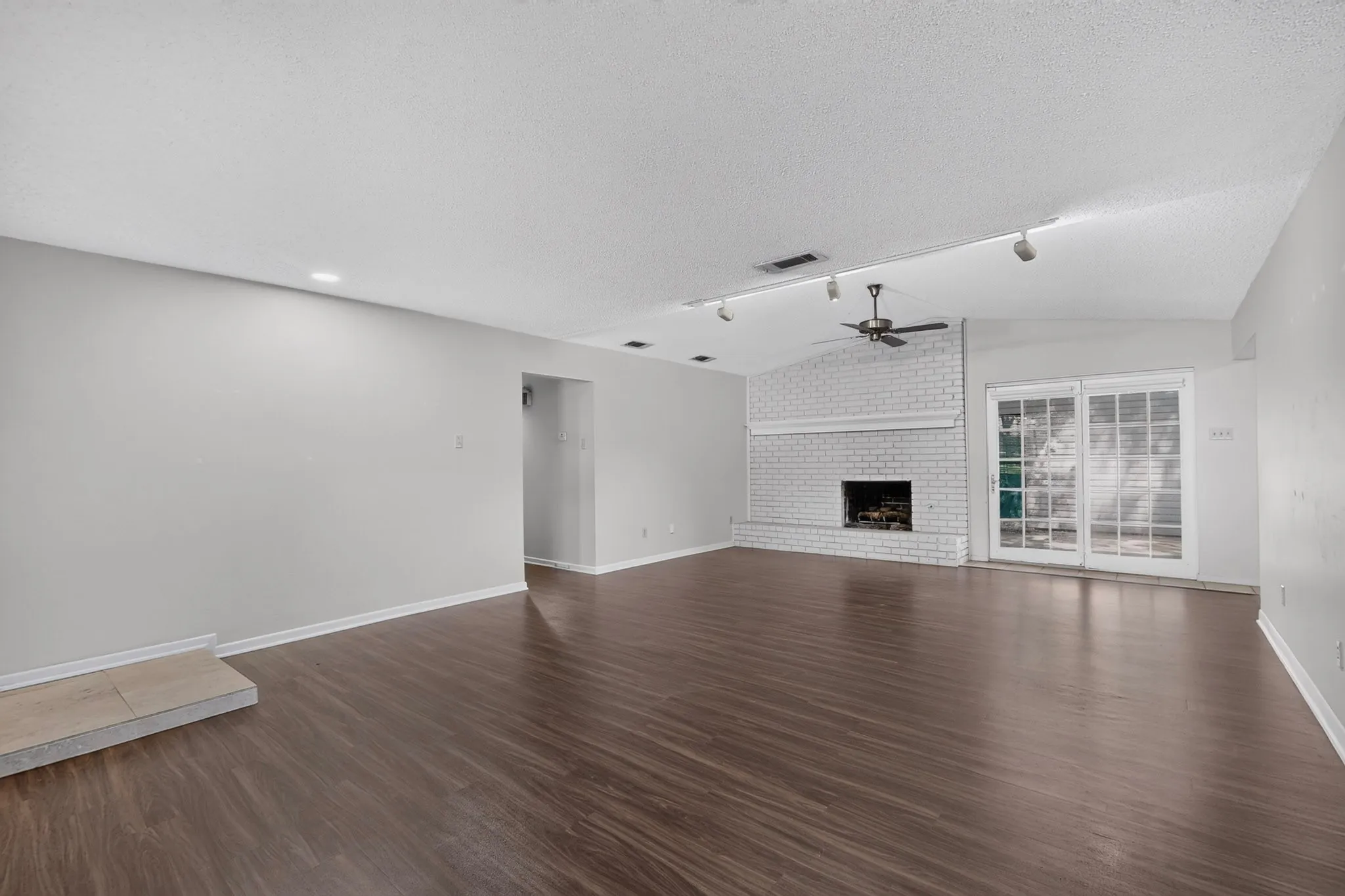 Vaulted ceiling with a ceiling fan, white brick fireplace, dark wood-finish flooring, recessed lighting, and sliding glass doors