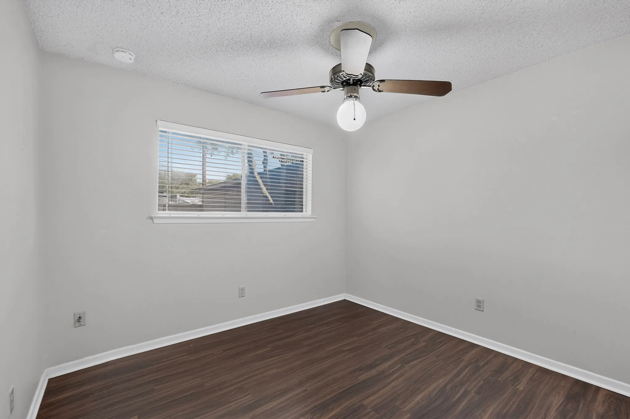 Wood-finish flooring, white baseboards, and a window with blinds