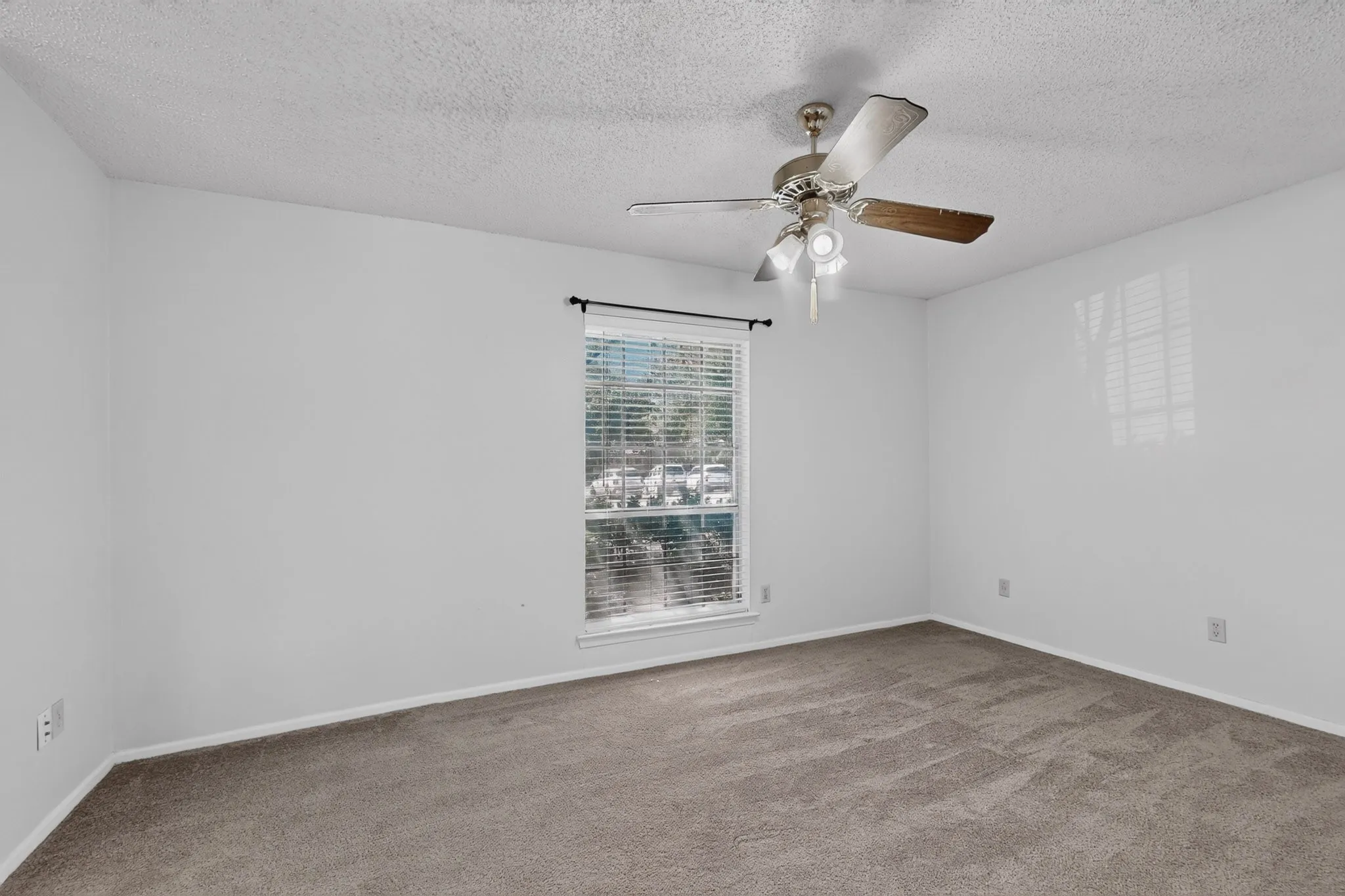 Spacious room featuring neutral carpeting, a single window with horizontal blinds, and a ceiling fan with integrated lighting