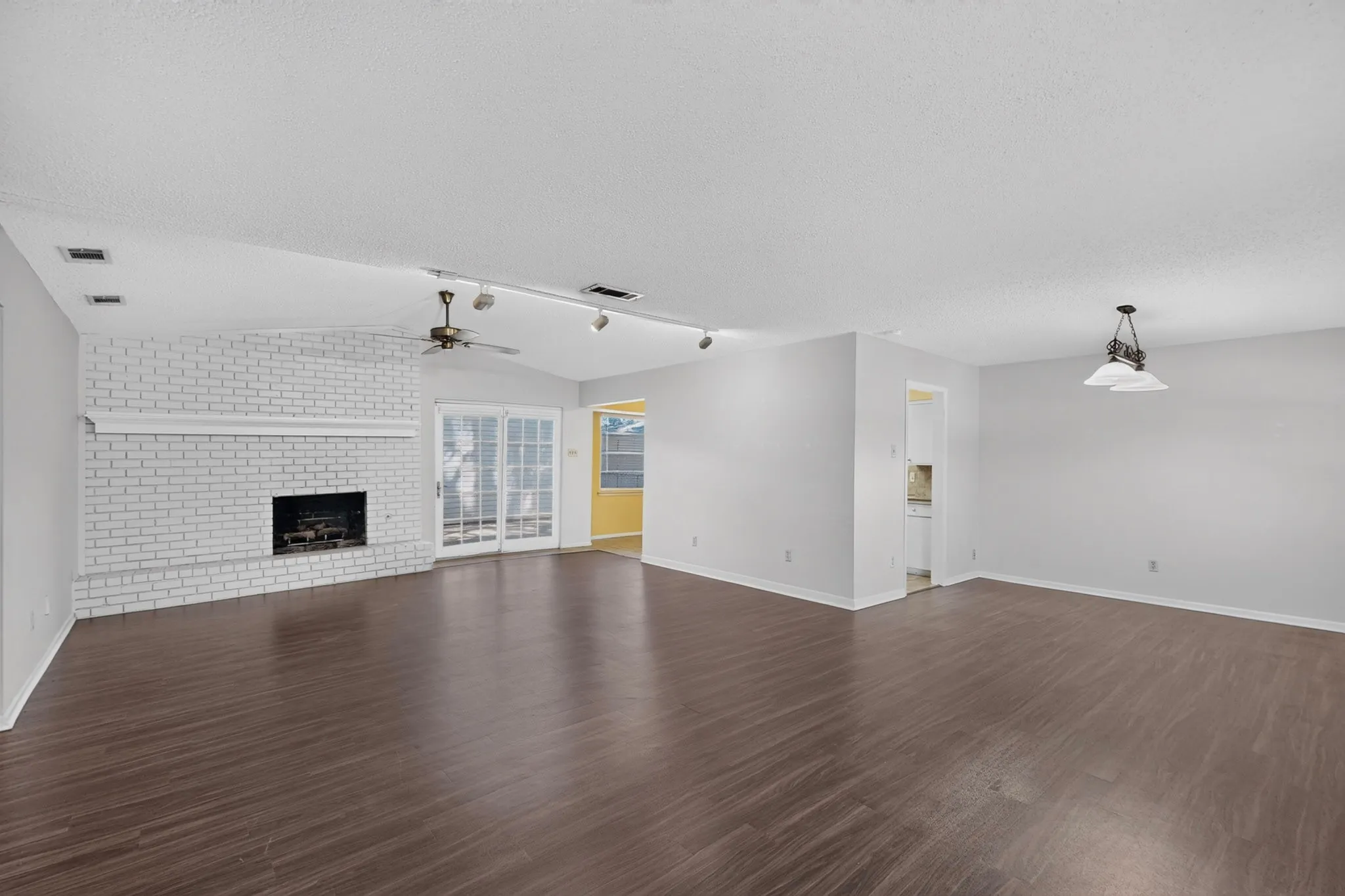 Wood-finish flooring throughout, white brick fireplace with a mantel, vaulted ceiling, ceiling fan, and double glass doors