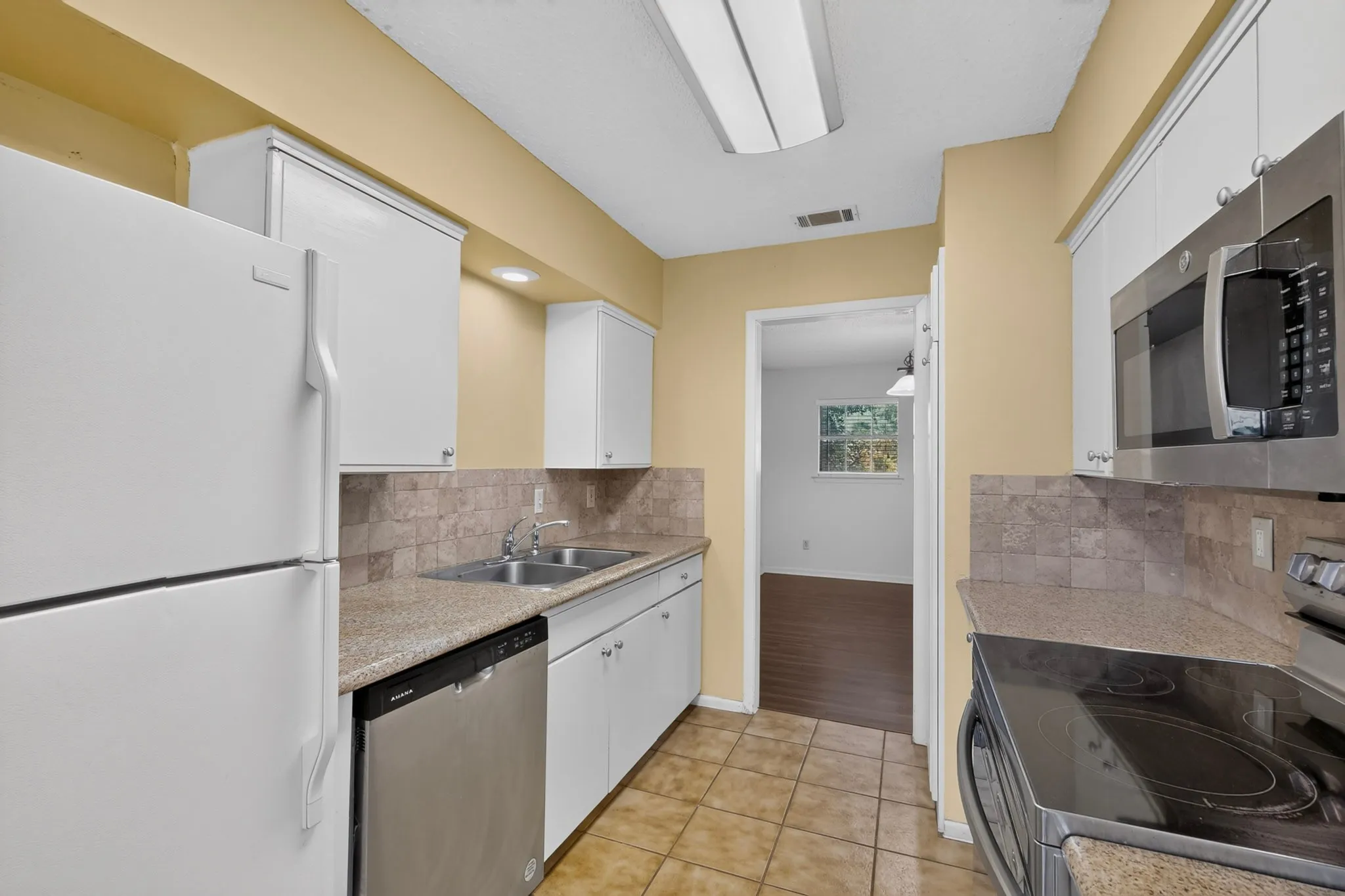 Kitchen featuring white cabinetry, tile flooring, stone-finish countertops, stainless steel appliances, and a tile backsplash