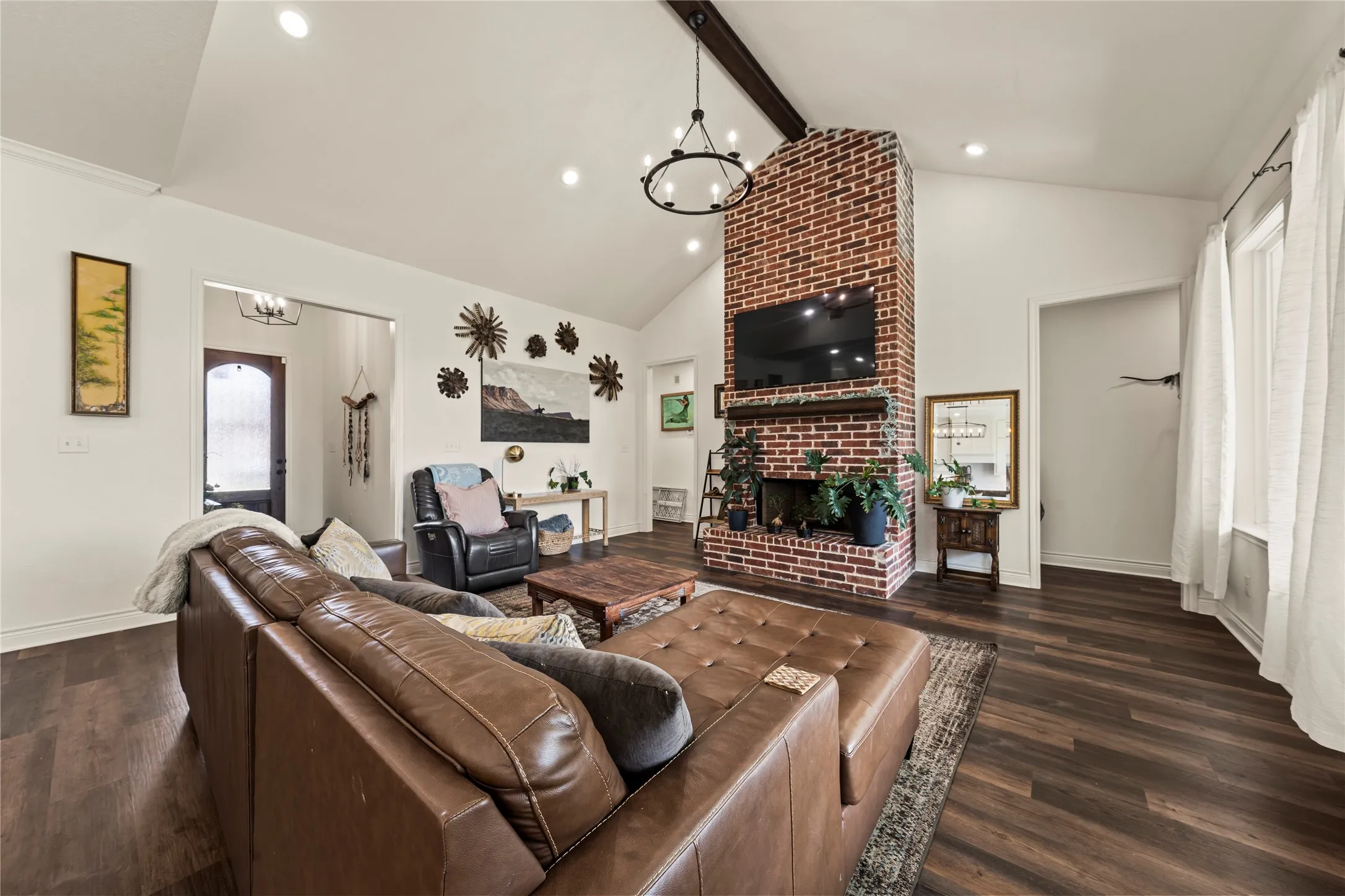 Vaulted ceiling with exposed wood beam, brick fireplace with wood mantel, recessed lighting, and wood-finish flooring