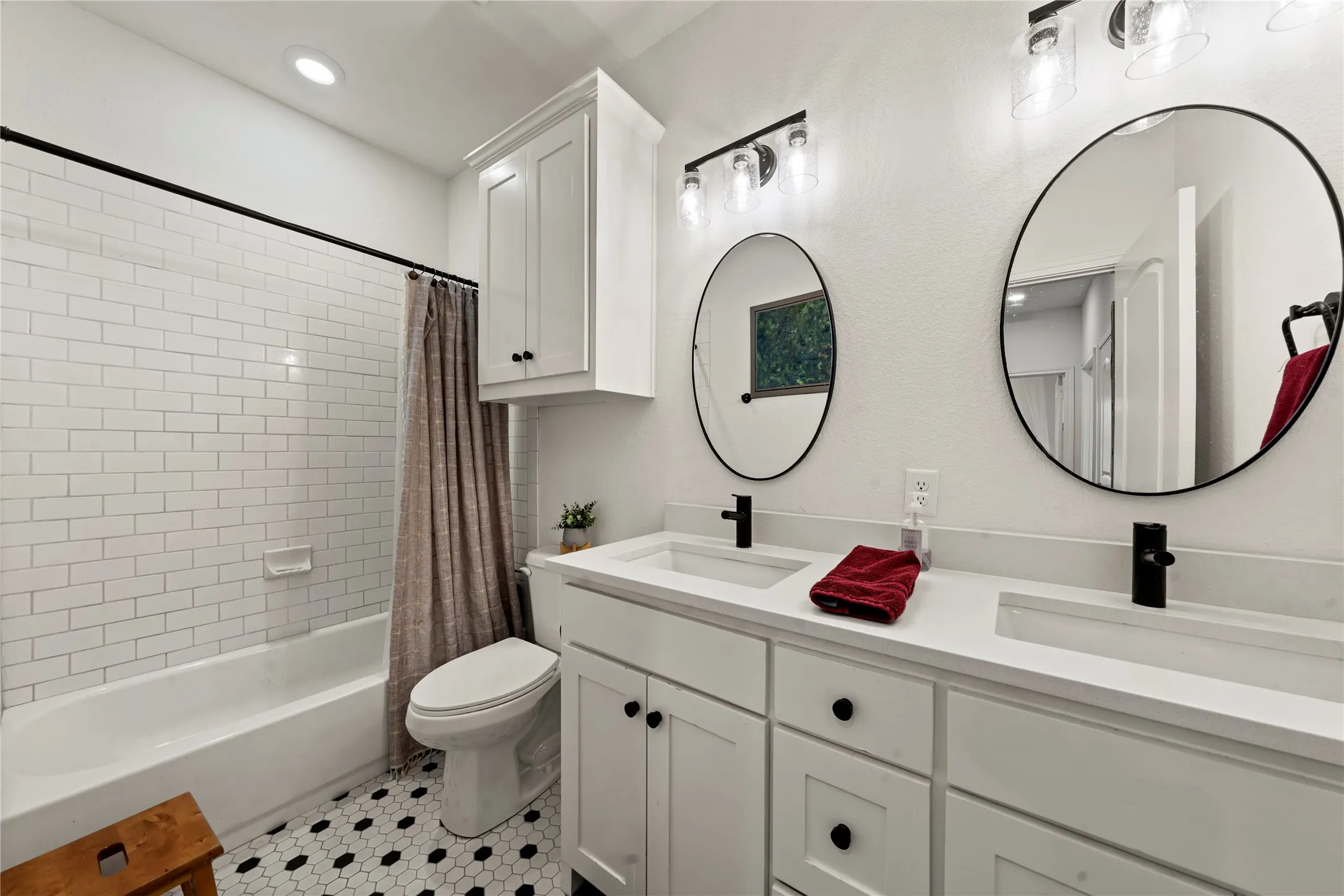 Dual vanity with undermount sinks and black fixtures, white cabinetry, and two round mirrors