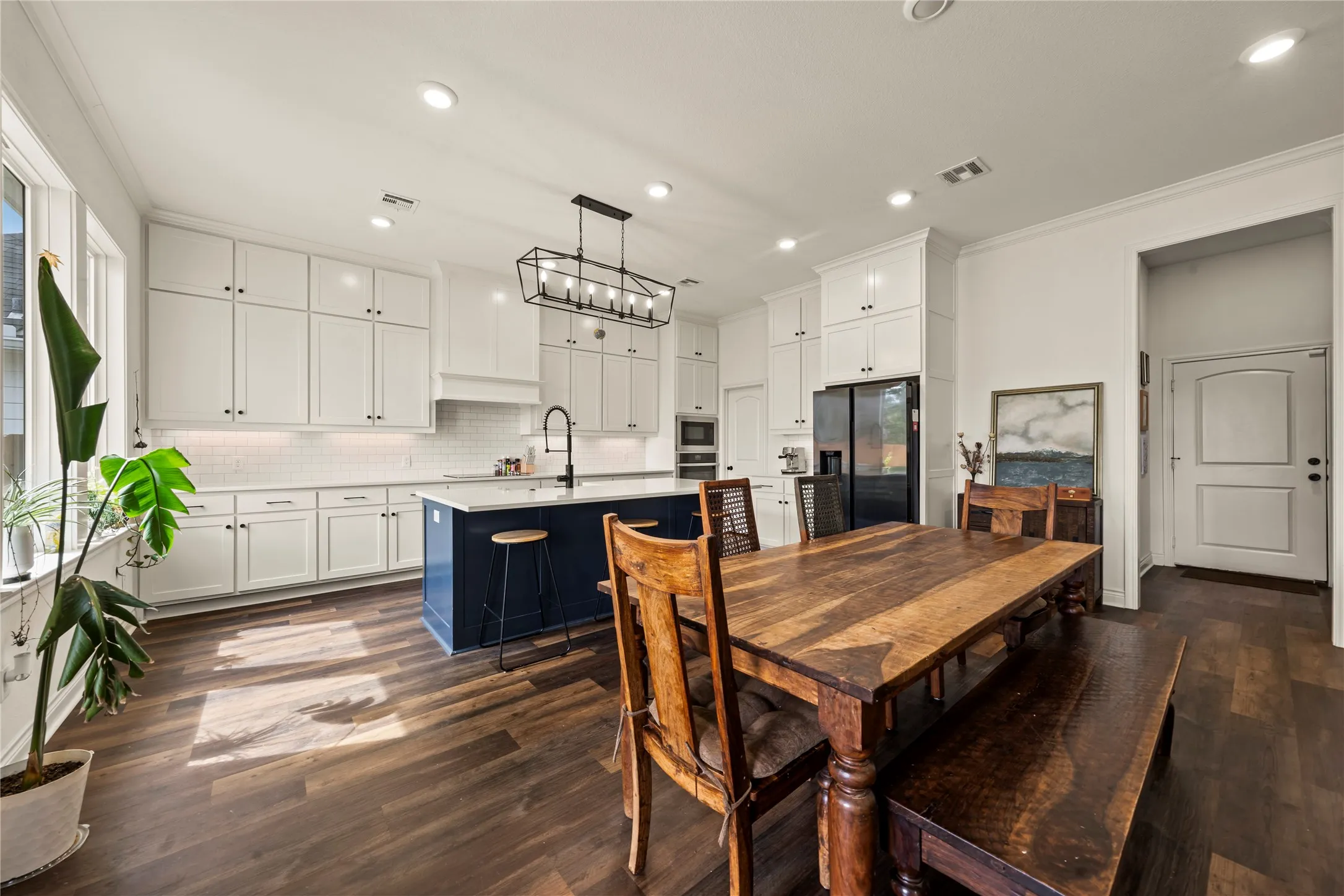 Spacious kitchen featuring white shaker cabinetry, an expansive island with a contrasting blue base, wood-finish flooring, a white subway tile backsplash, and recessed lighting