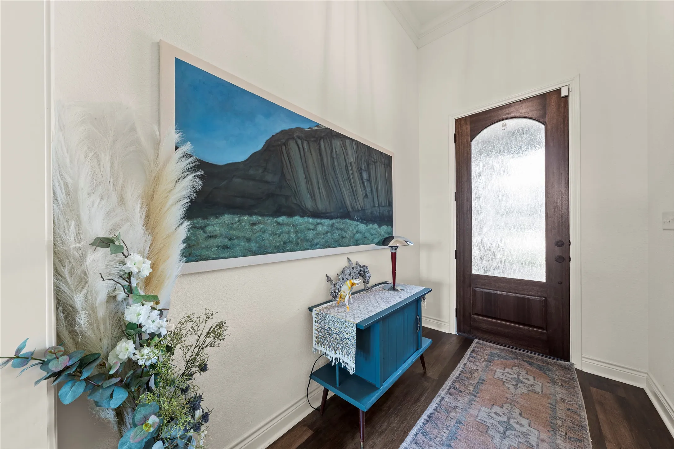 Arched wood door with frosted glass panel, crown molding, and wood-finish flooring