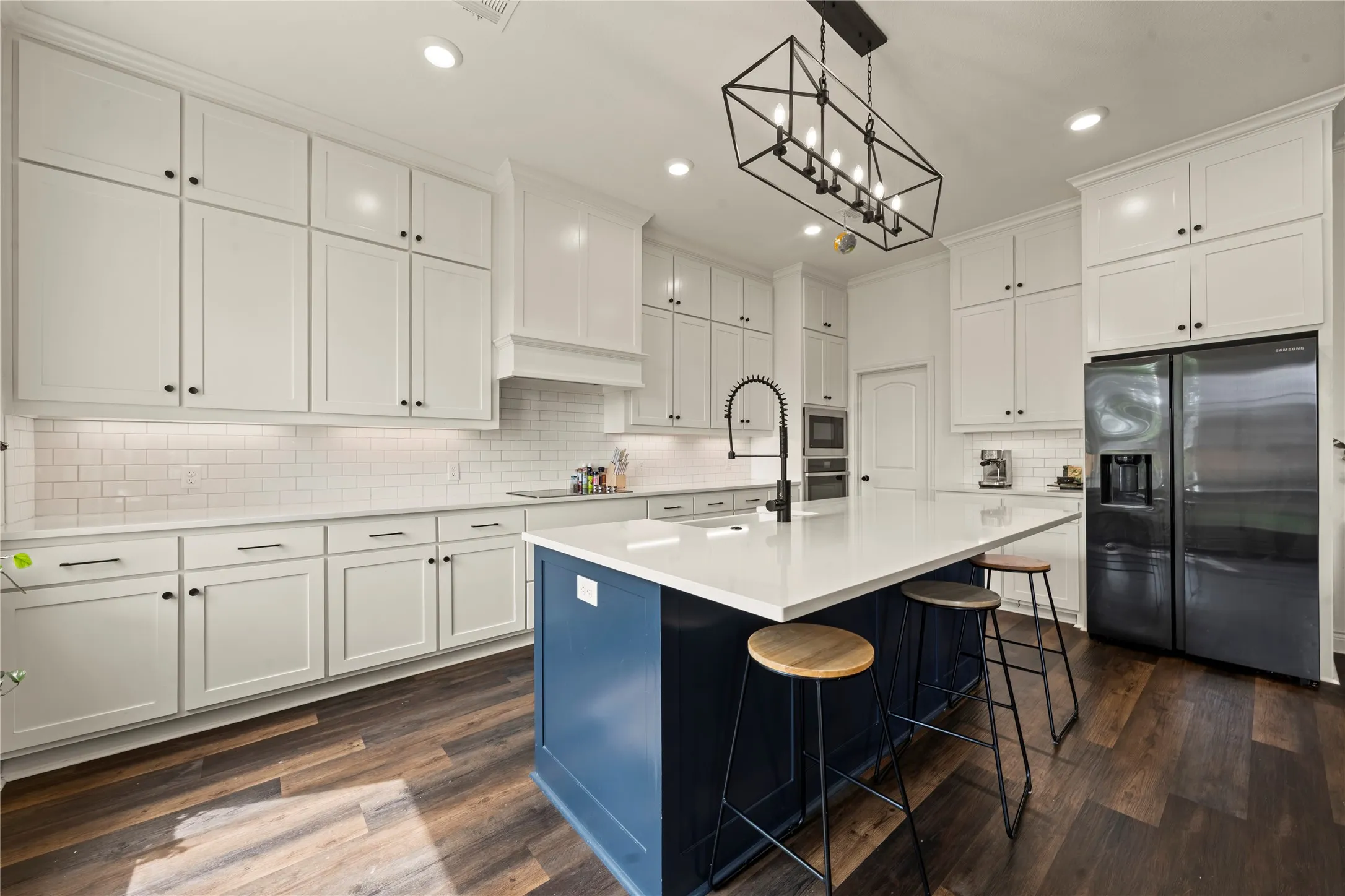 Expansive kitchen featuring a large central island with seating, white shaker cabinetry, wood-finish flooring, and a subway tile backsplash