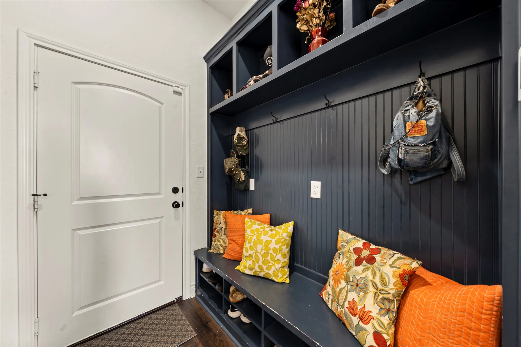 Built-in storage bench with cubbies, beadboard paneling, integrated hooks, and overhead shelving