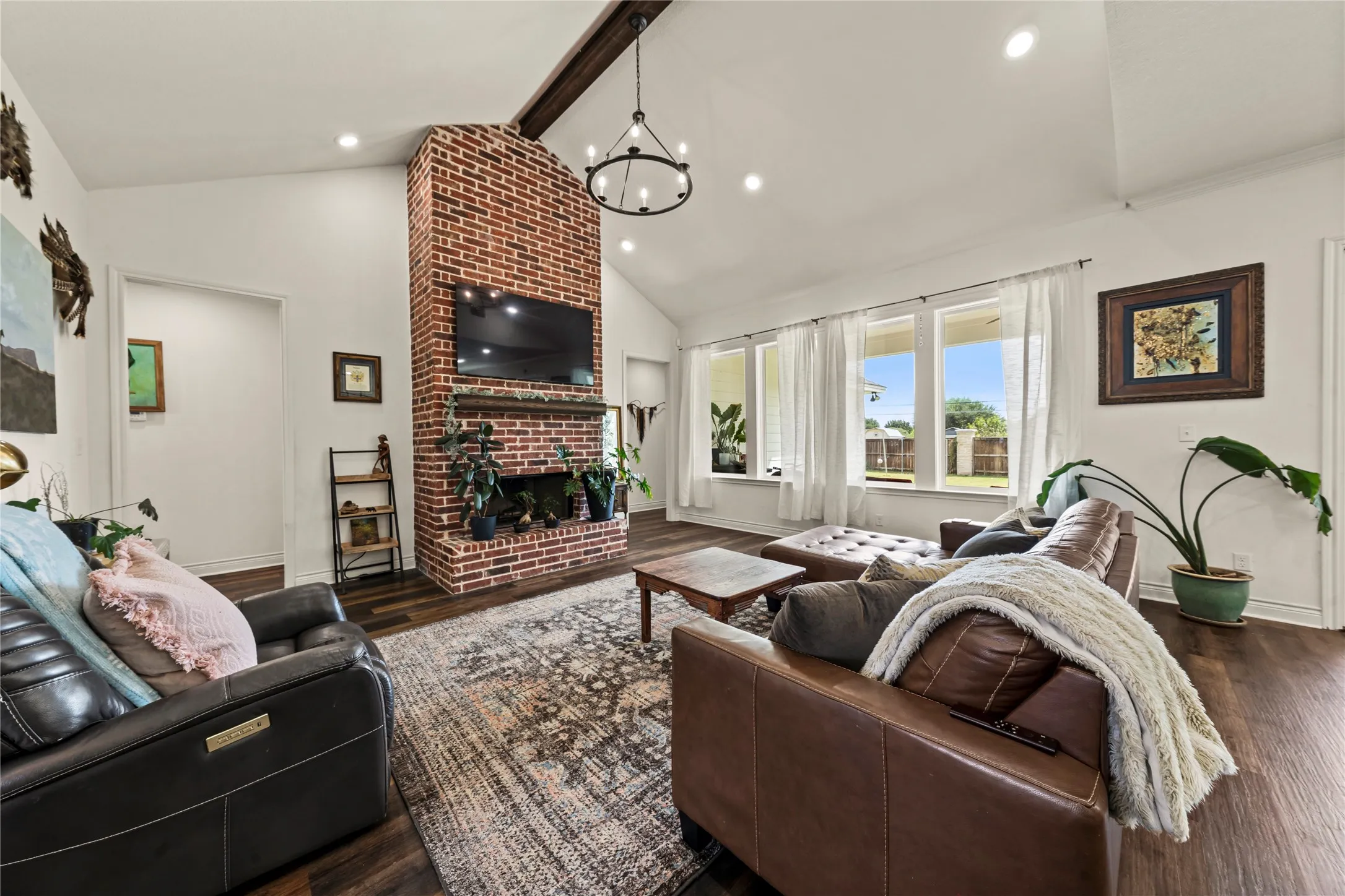 Vaulted ceilings with exposed wood beam, a brick-clad fireplace, wood-finish flooring, and multiple windows providing natural light
