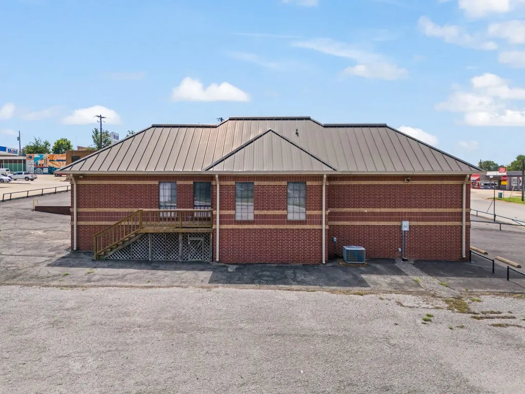 Brick exterior with a metal roof, featuring multiple windows, a wooden deck, and an exterior staircase