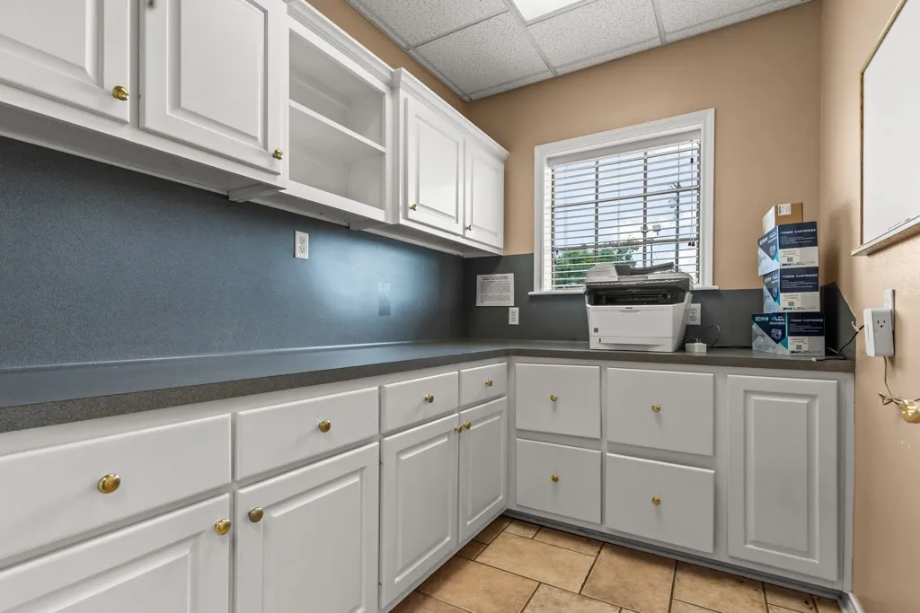 White cabinetry with brass hardware, solid surface countertops, and tile flooring