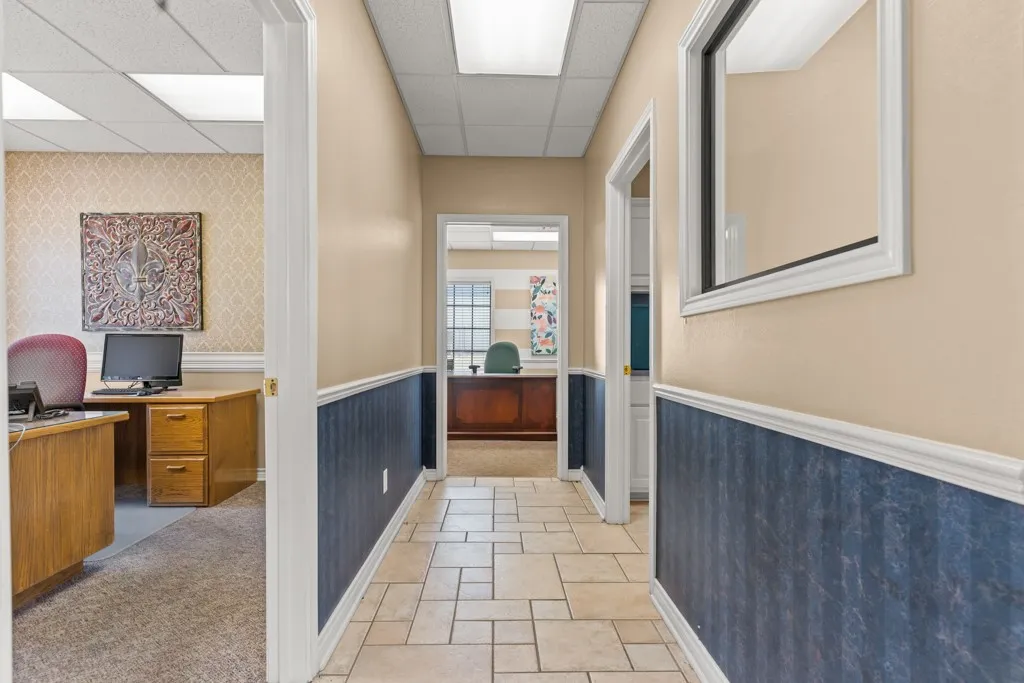 Hallway with light-colored tile flooring, overhead fluorescent lighting, and wainscoting
