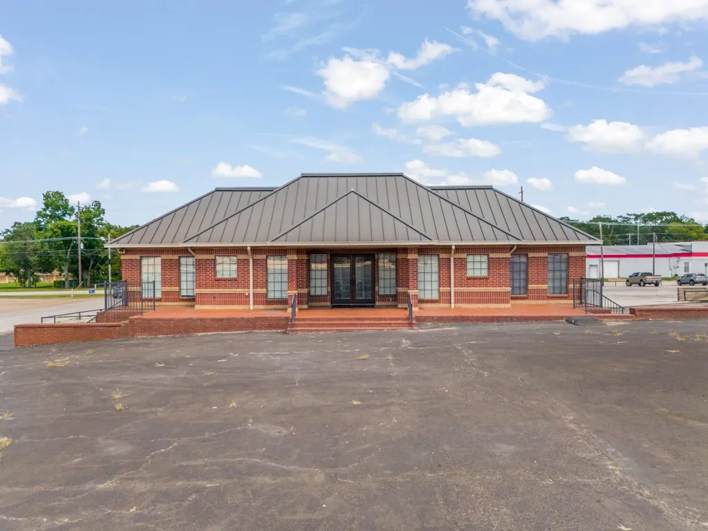Brick exterior with a dark metal standing seam roof, multiple large windows, and a paved parking area